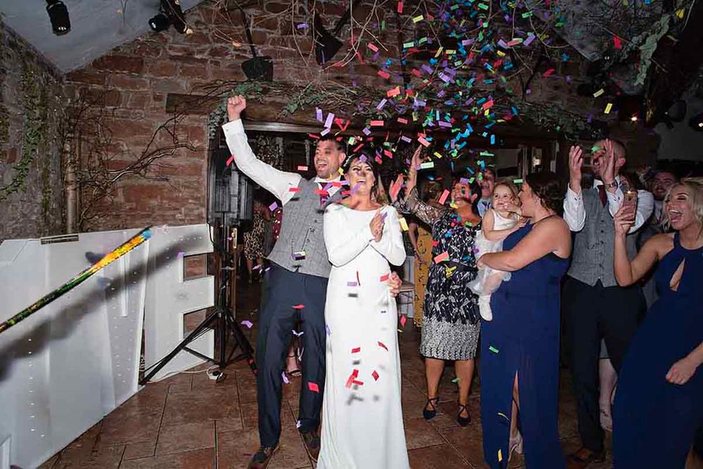 Bride and groom celebrate with colorful confetti cannons surrounded by joyful wedding guests at Skitby House