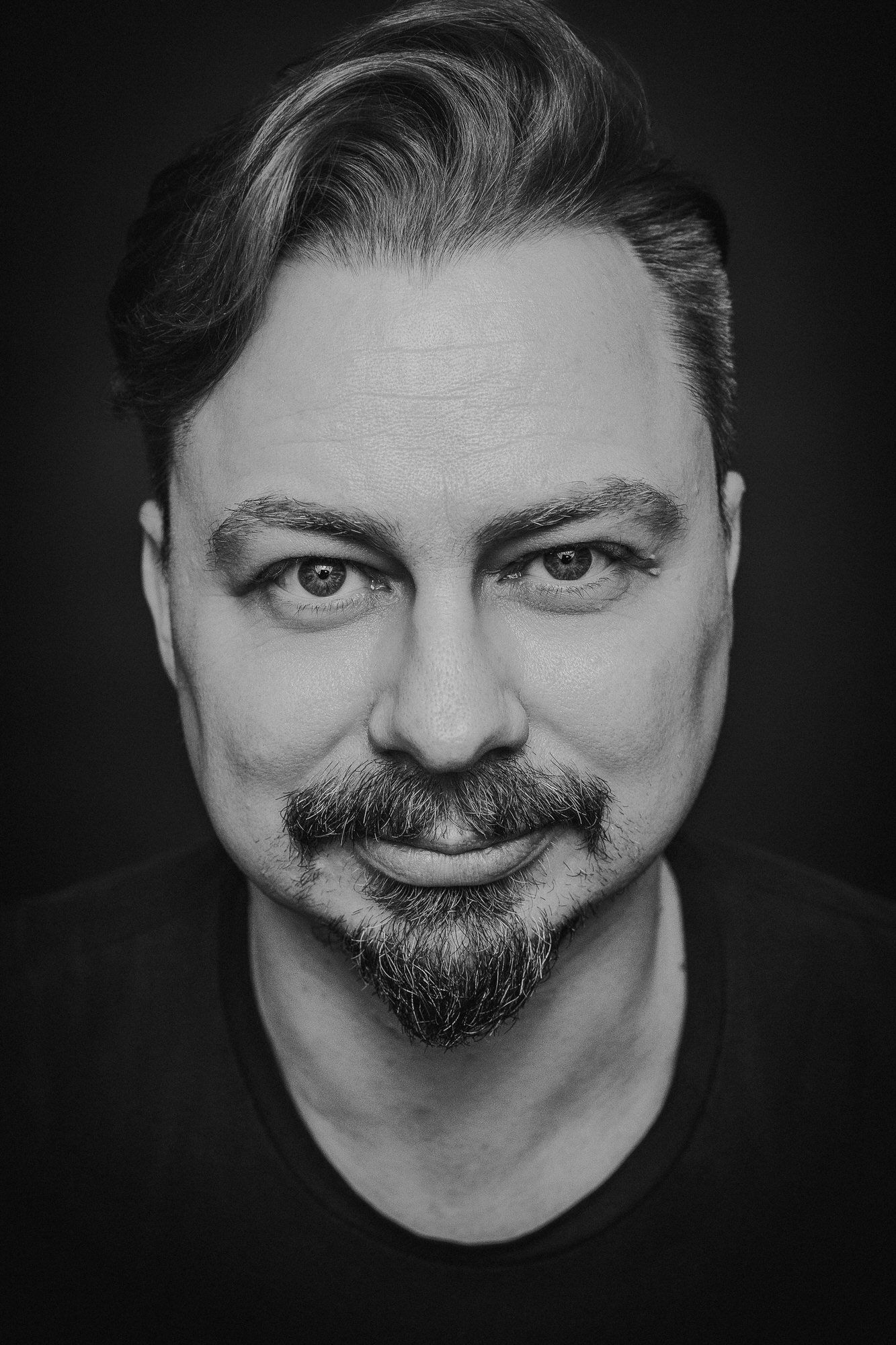 Black and white portrait of a middle-aged man with a goatee and styled hair, smiling confidently at the camera.