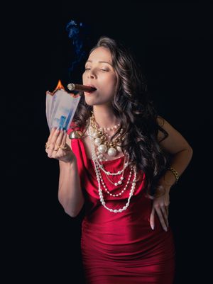 Woman in red dress and pearl necklaces smoking cigar while burning money against black background.