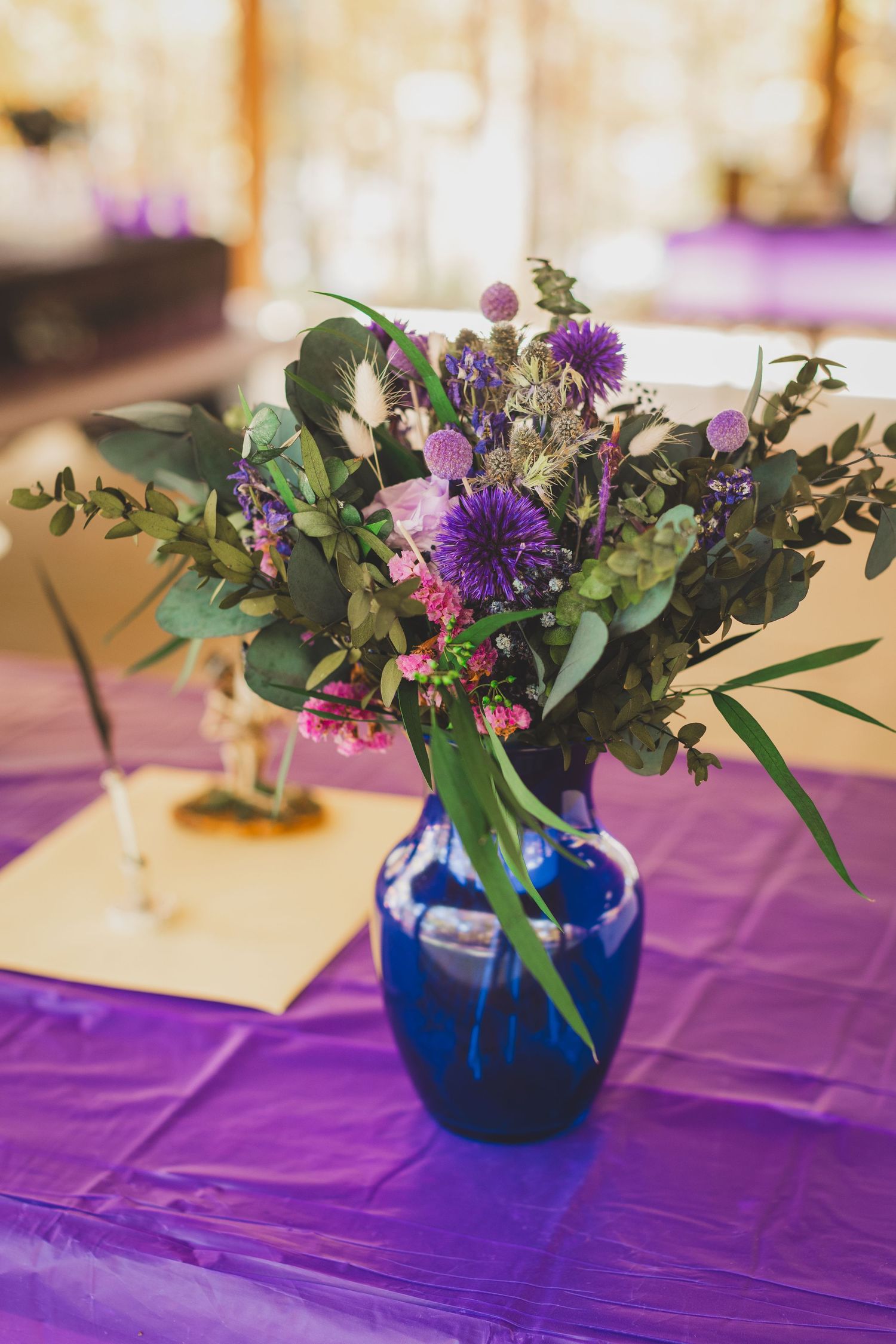 Blue vase with purple wildflowers and greenery on a purple tablecloth at an elegant event.