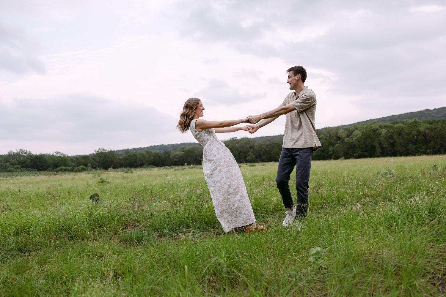 Couple standing together in a sunlit rocky landscape surrounded by green trees during golden hour outdoor photoshoot.