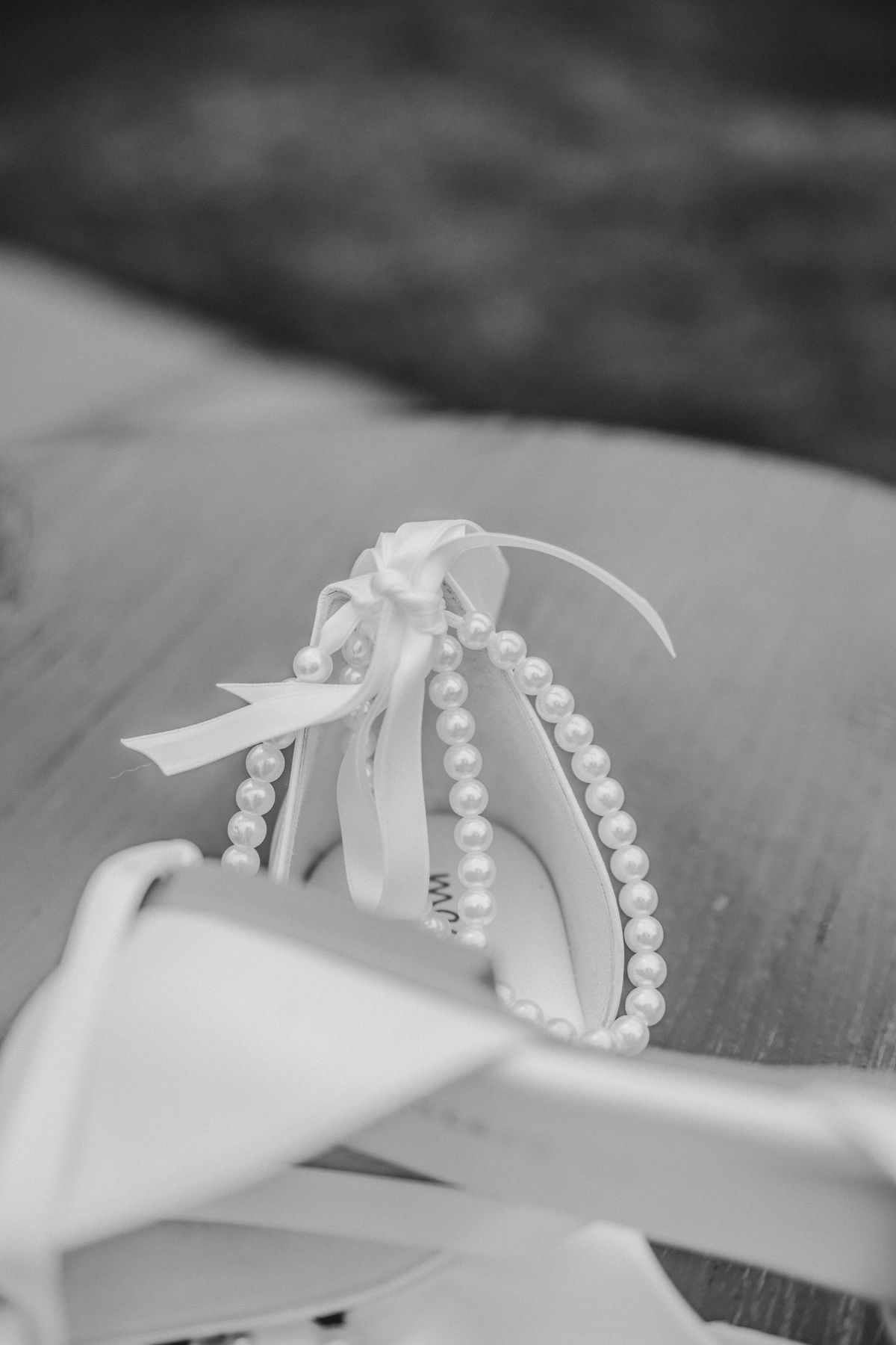 Black and white photo of elegant bridal garter with pearl beading and satin ribbon bow on wooden surface.