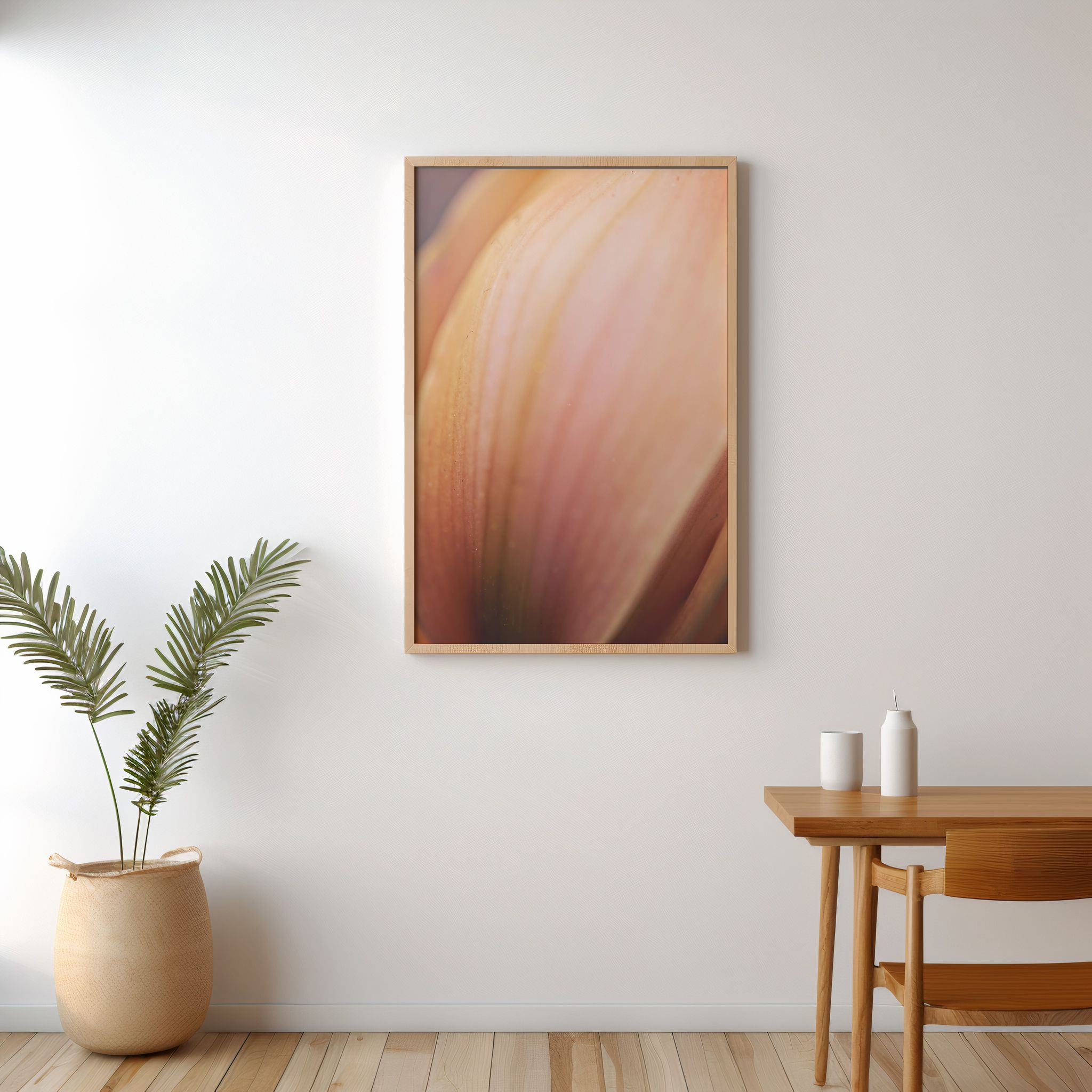 Framed close-up floral art print in warm pink and peach tones, displayed on a white wall above a wooden table.