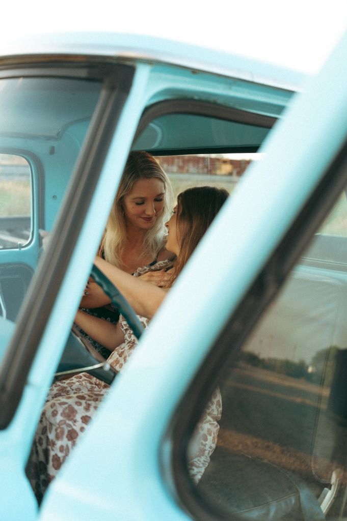 Two women sharing a tender moment inside a vintage light blue truck, viewed through the window in Prosper TX