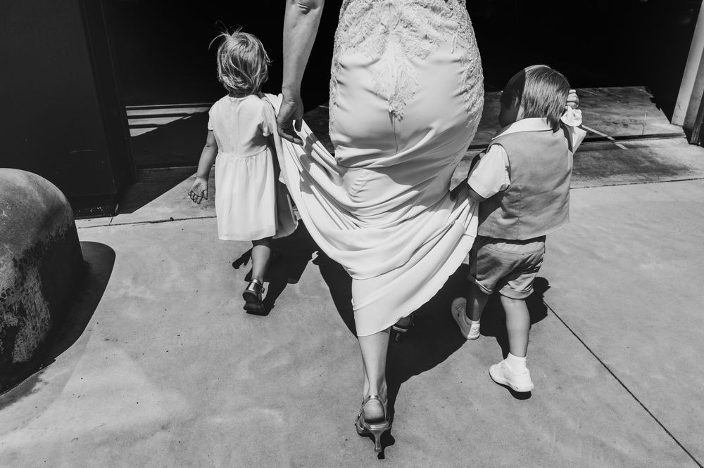 Spontane huwelijksfoto in zwart wit van twee kinderen die de sleep van de bruid dragen, door huwelijksfotograaf Bart Boodts.