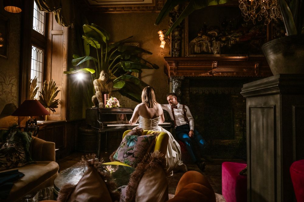 Sfeervolle huwelijksfoto van een koppel aan de piano in een stijlvol interieur, door huwelijksfotograaf Bart Boodts.