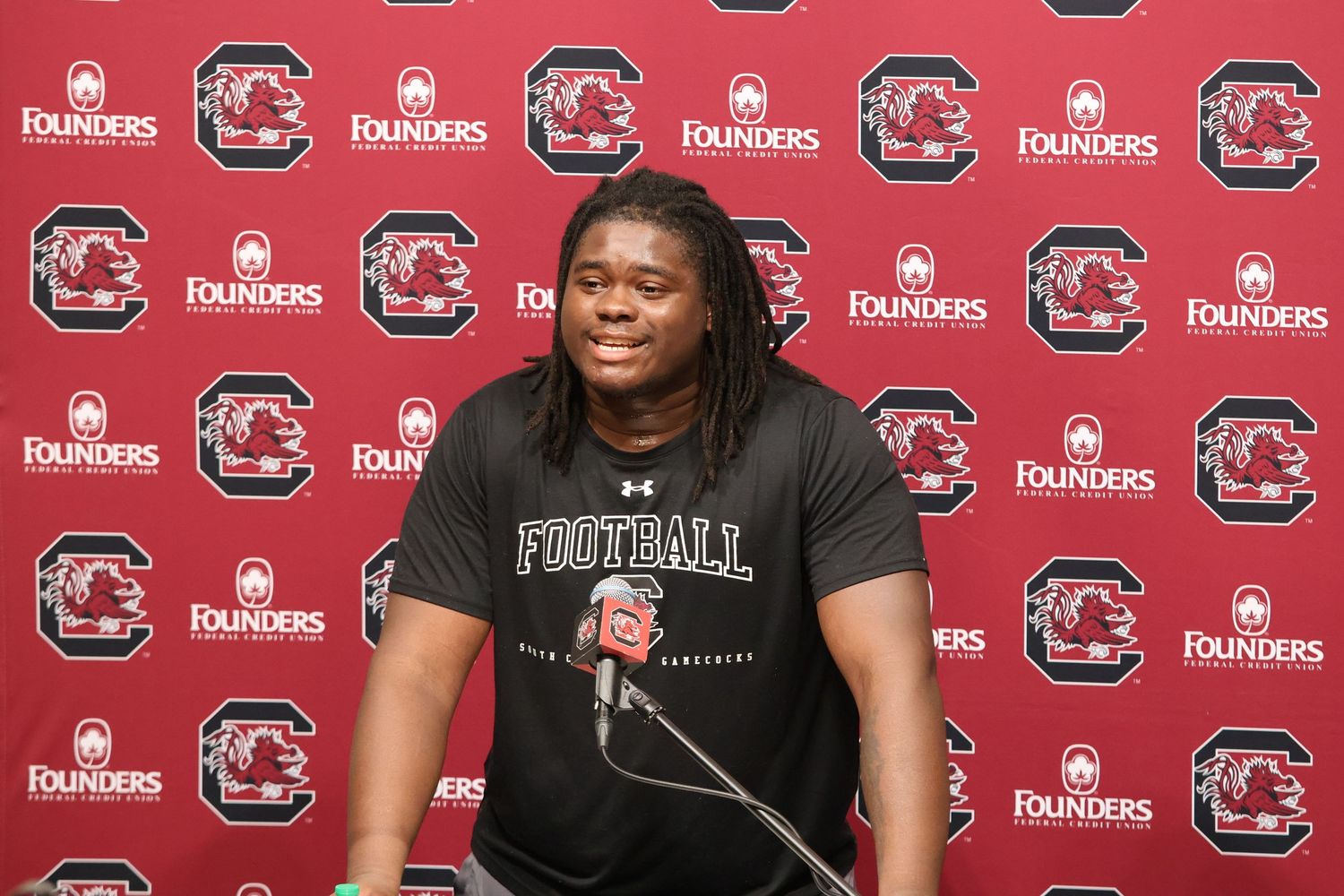 South Carolina football player speaks at a press conference in a black team shirt.
