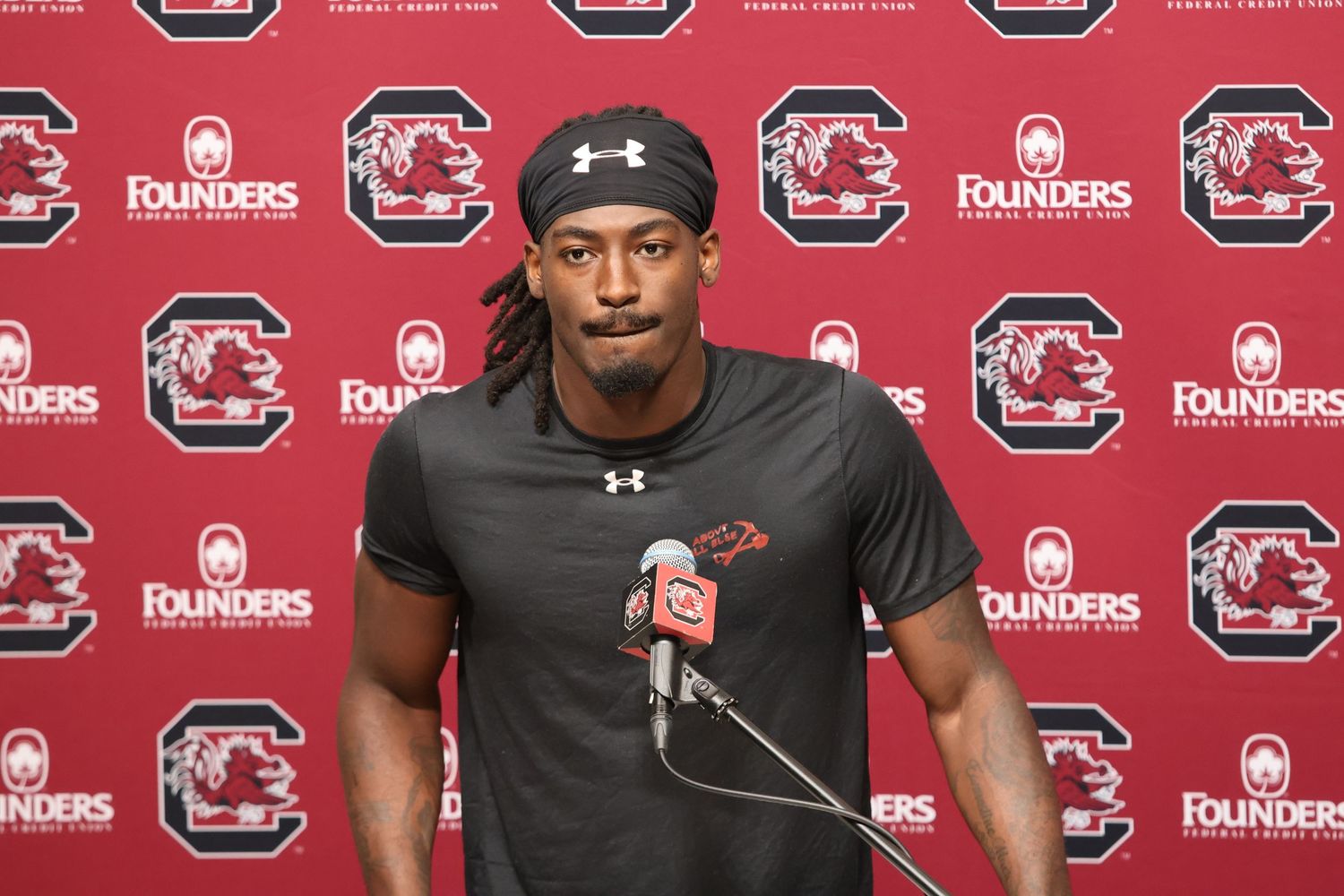 South Carolina football player wearing a headband addresses reporters at a podium.