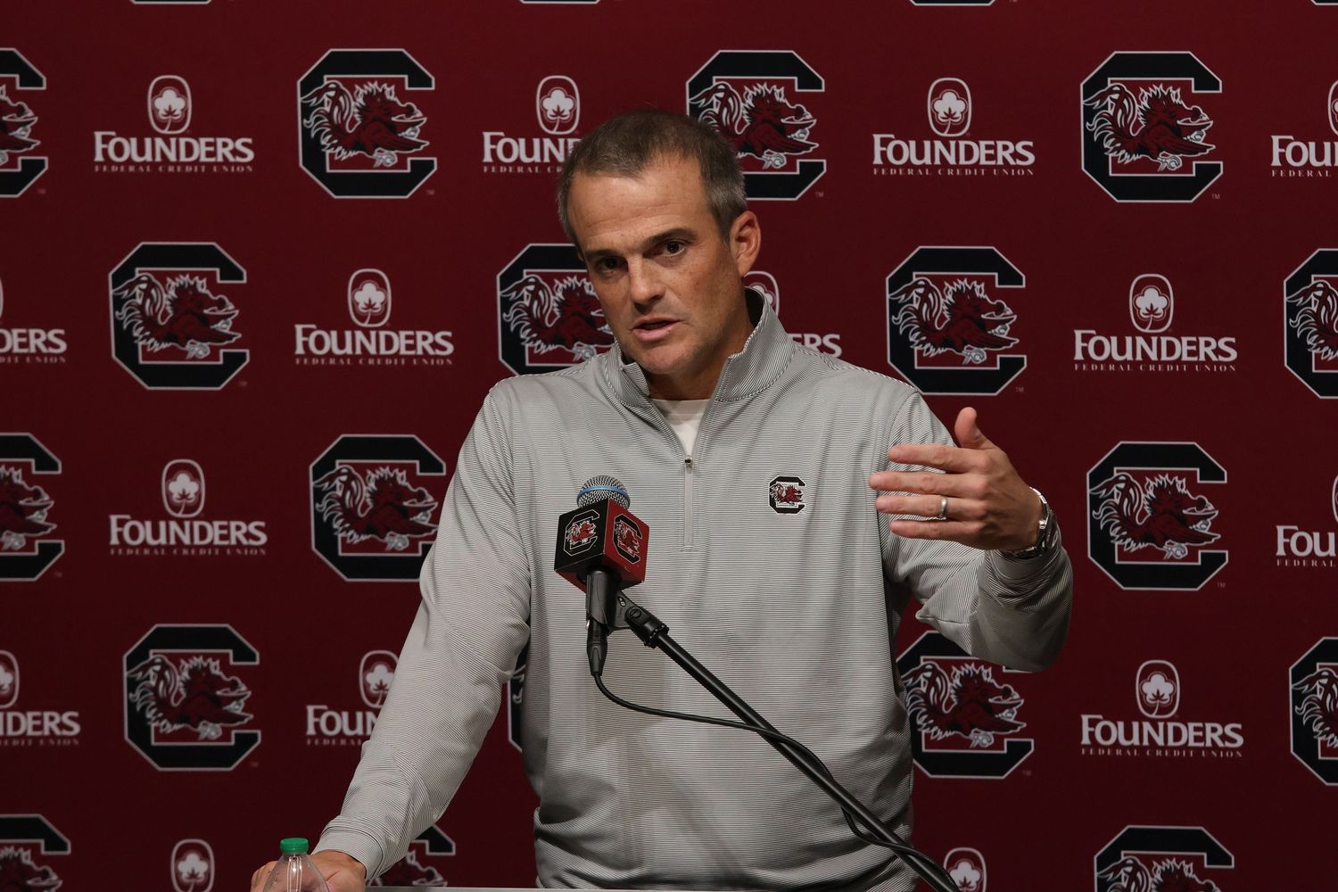 South Carolina football coach gestures while speaking at a press conference podium.
