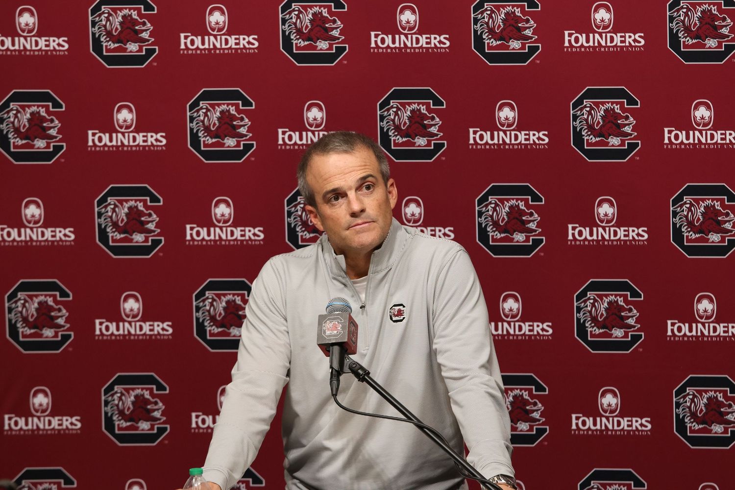 South Carolina football coach listens at a press conference podium.