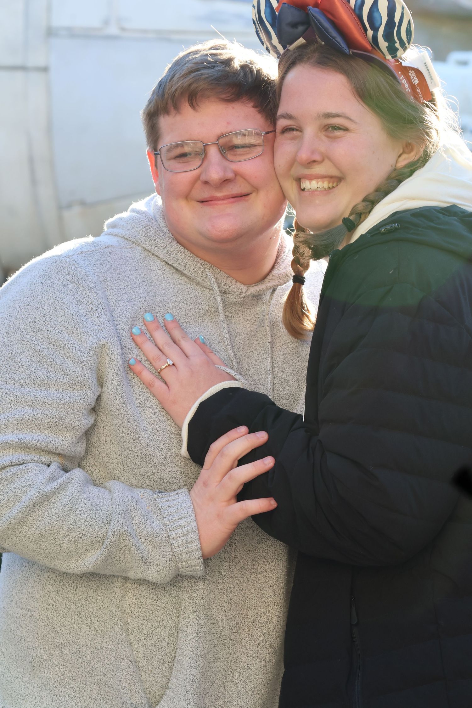 Smiling couple poses closely together outdoors in bright sunlight.