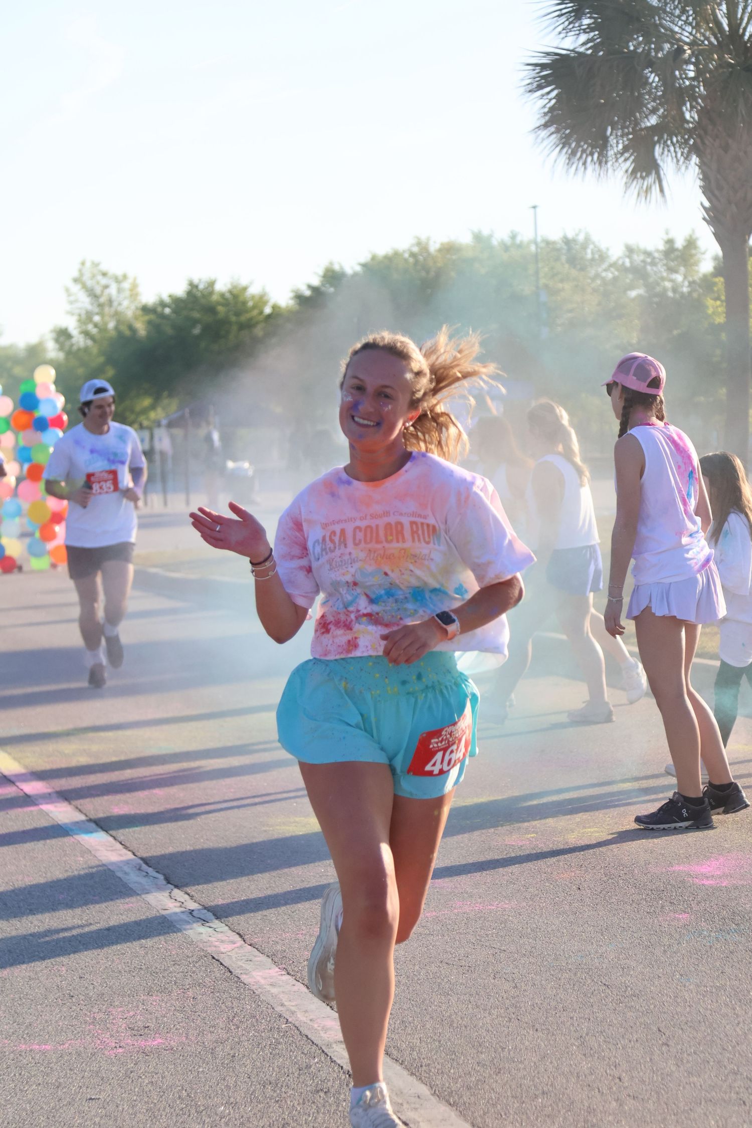 Smiling runner waves while moving through colorful powder at a color run.