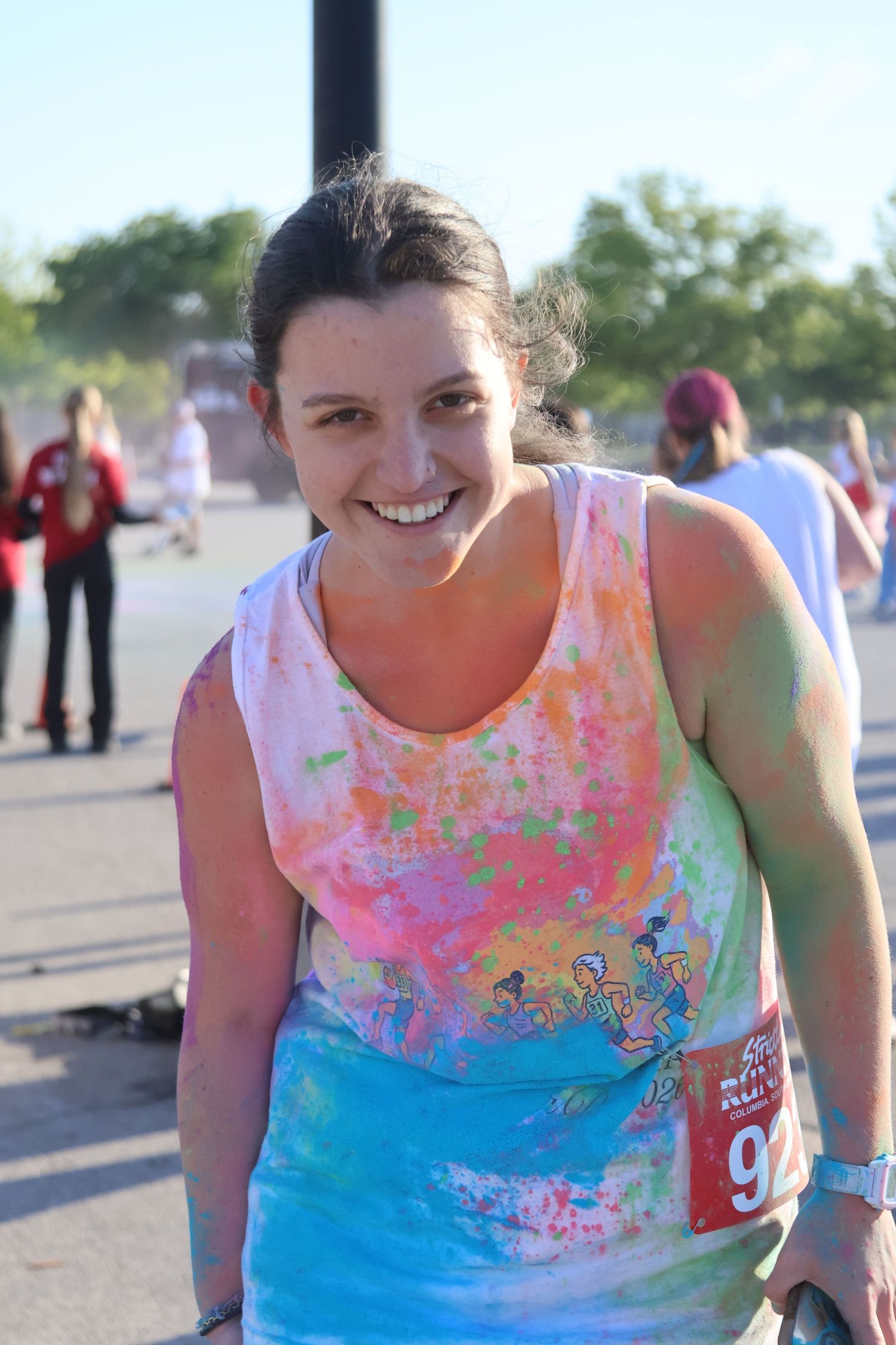 Color-run participant smiles at the camera with bright powder covering her shirt and arms.