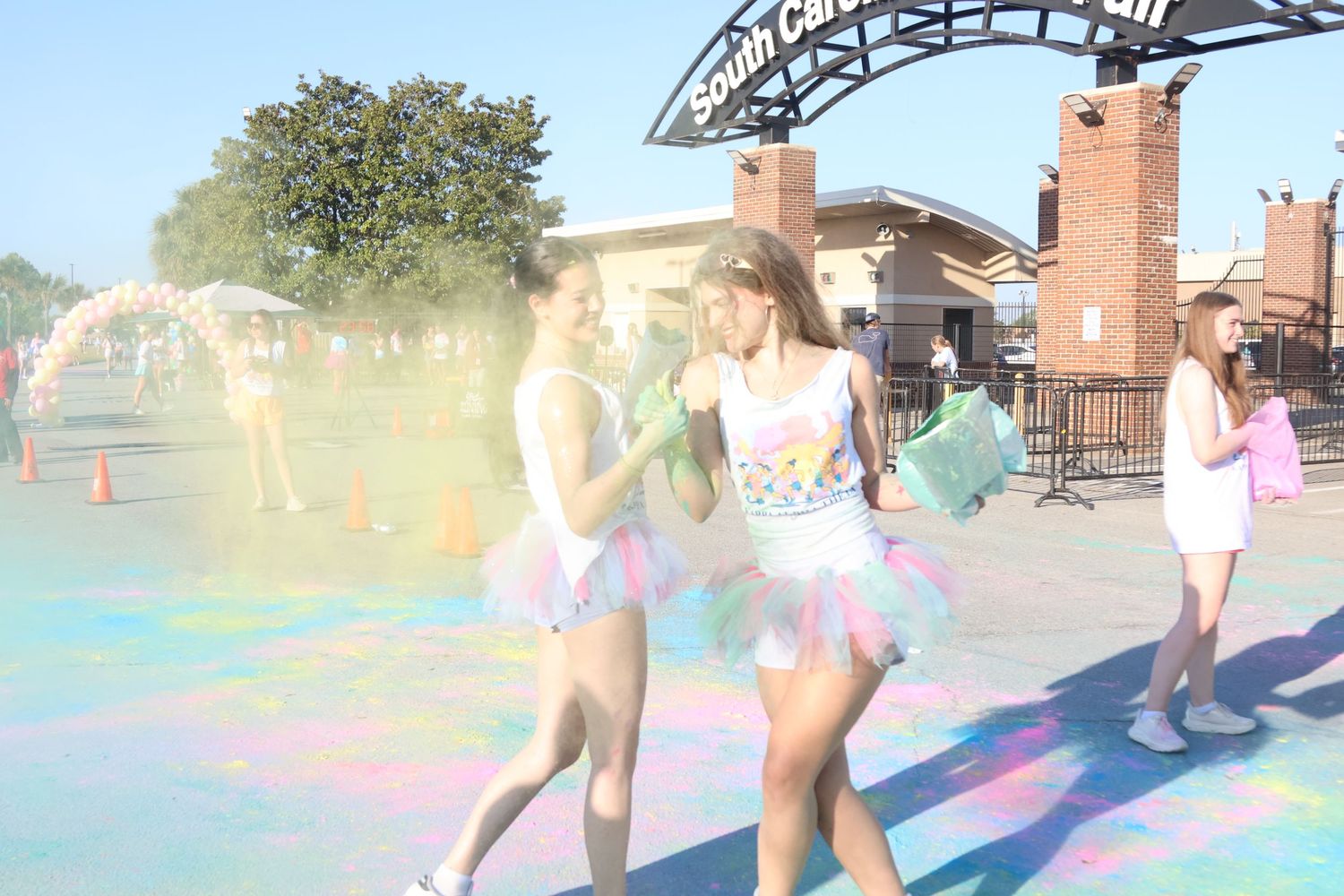 Two smiling runners pass through a cloud of colored powder at a color run.