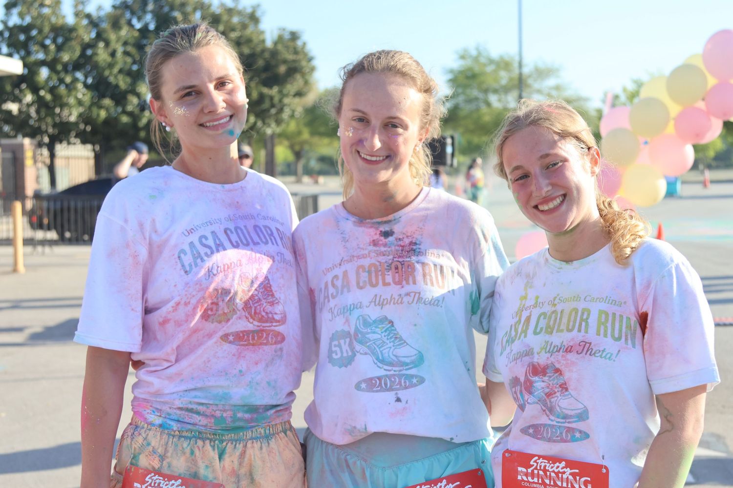 Three color-run participants smile together in powder-stained shirts after the event.