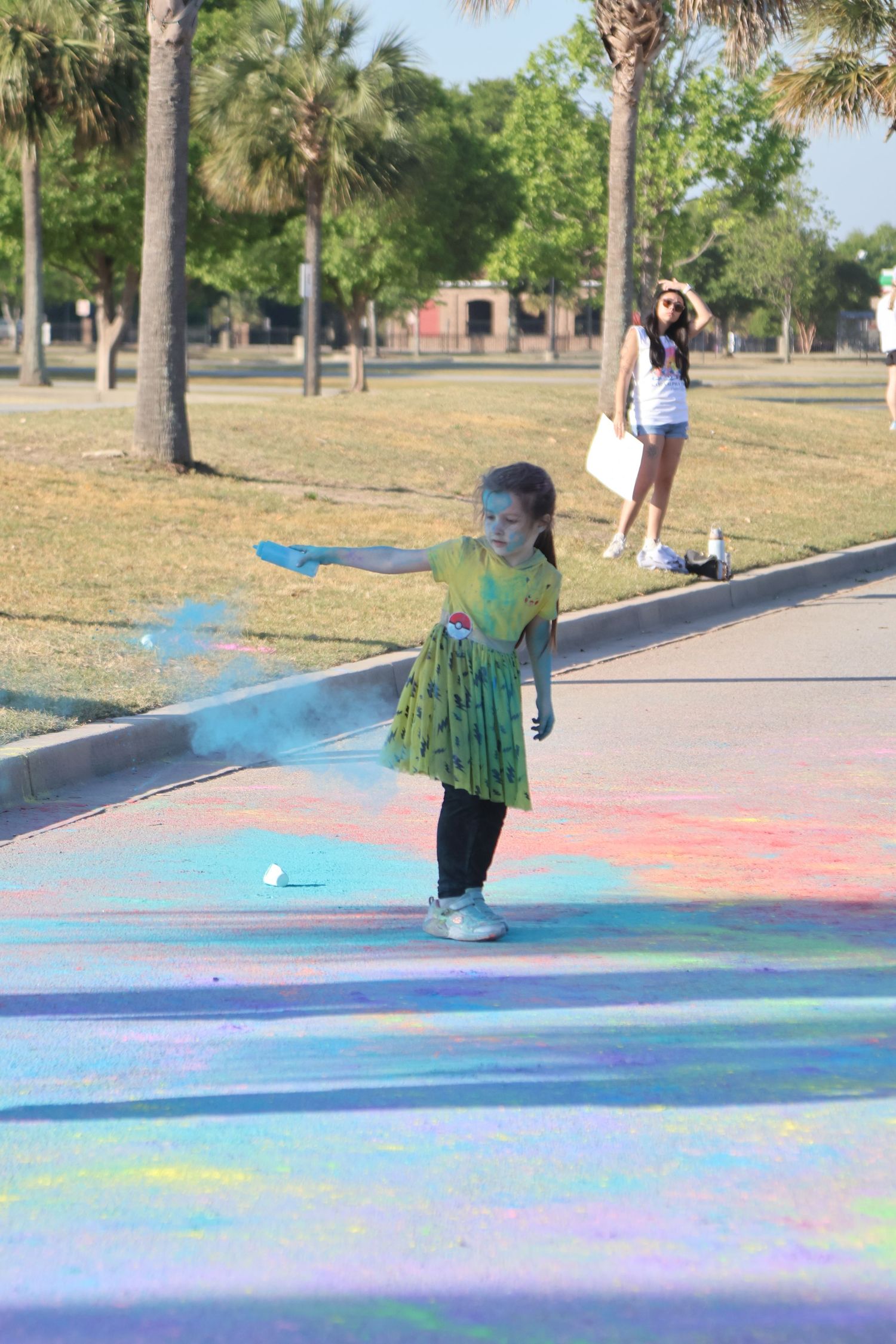 Young child throws blue powder across a brightly colored street during a color run.