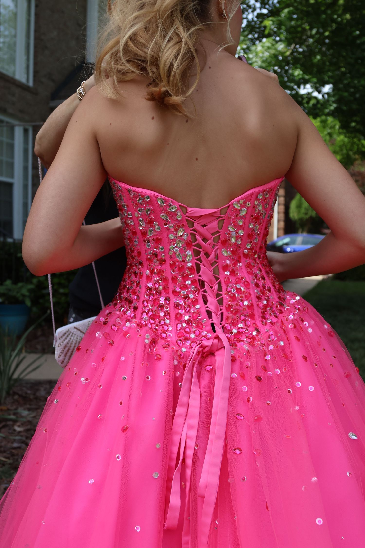 Close-up of the jeweled lace-up back and ribbon of a bright pink prom gown.