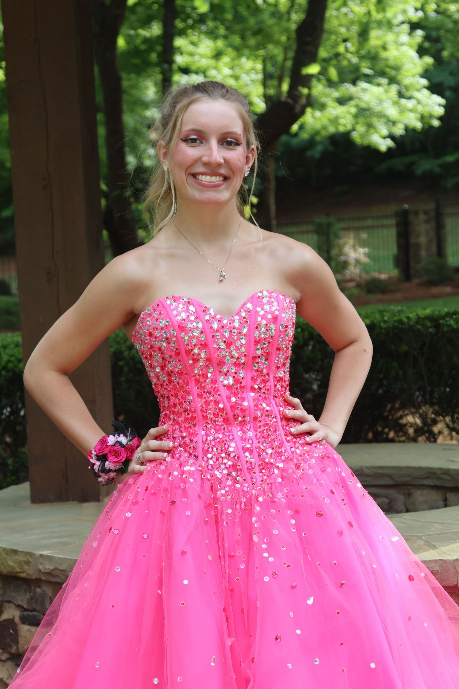 Teen poses with hands on her hips in a jeweled bright pink prom gown.