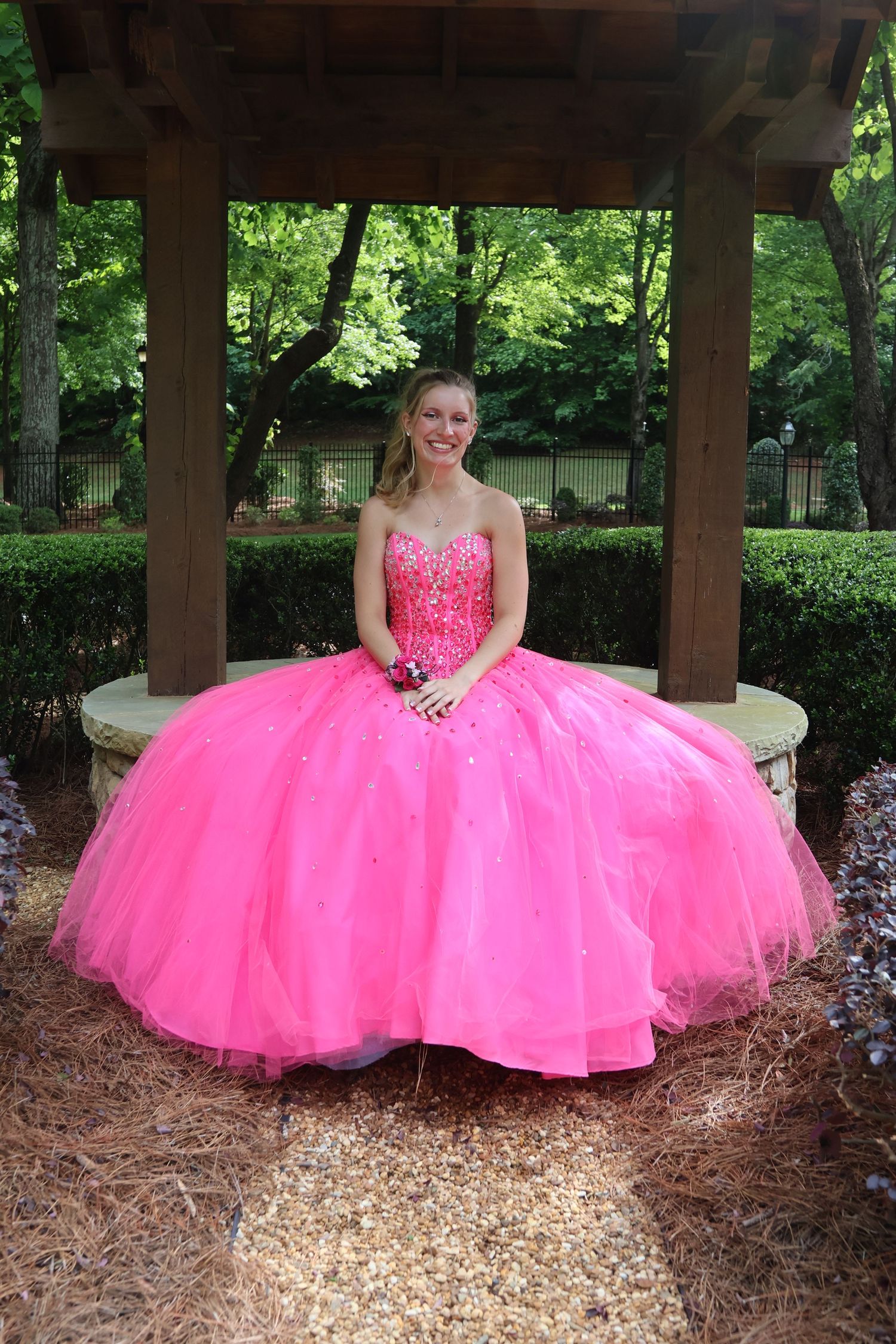Teen in a bright pink ball gown sits beneath a wooden garden pavilion.