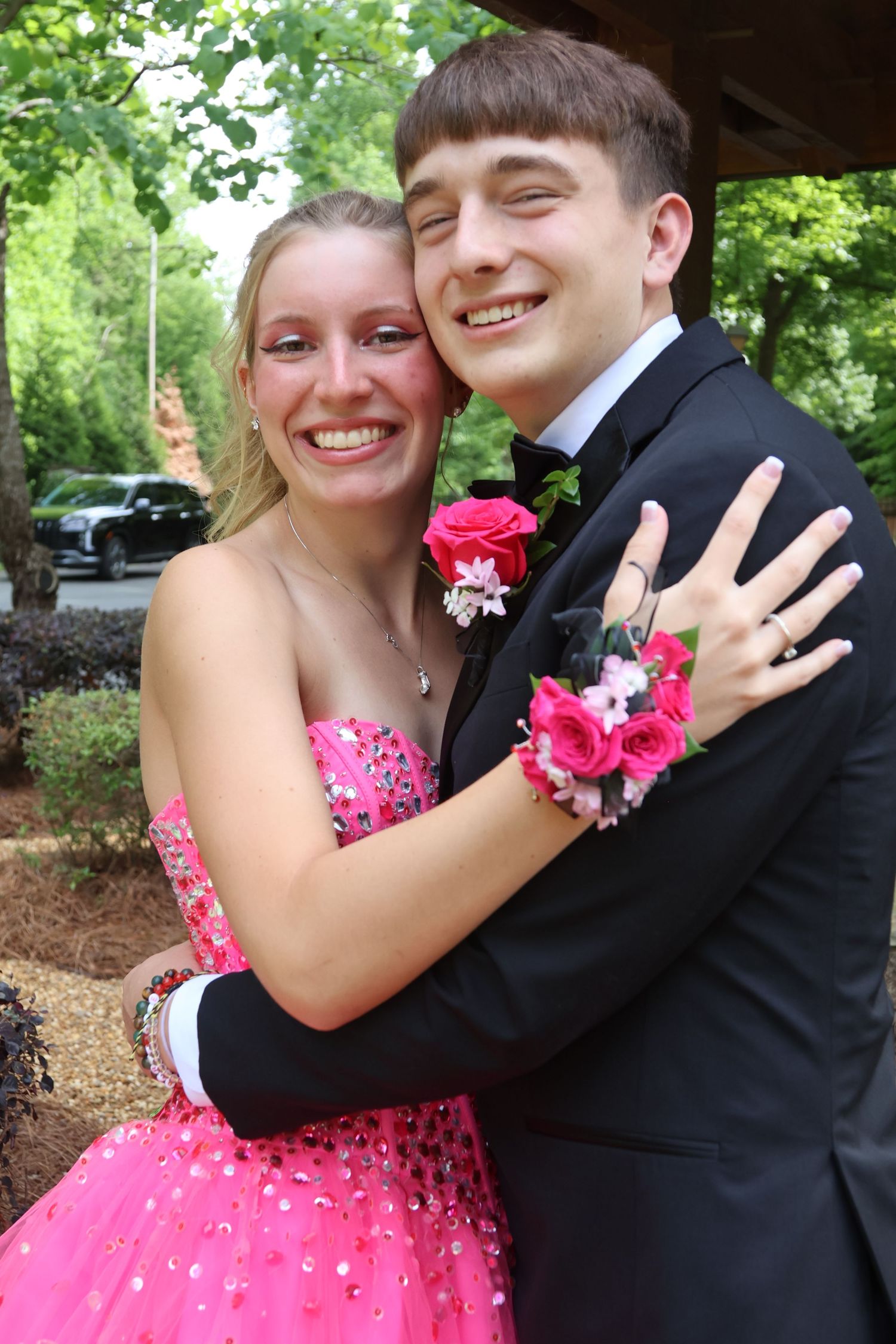 Smiling prom couple embraces outdoors in coordinated pink and black formalwear.