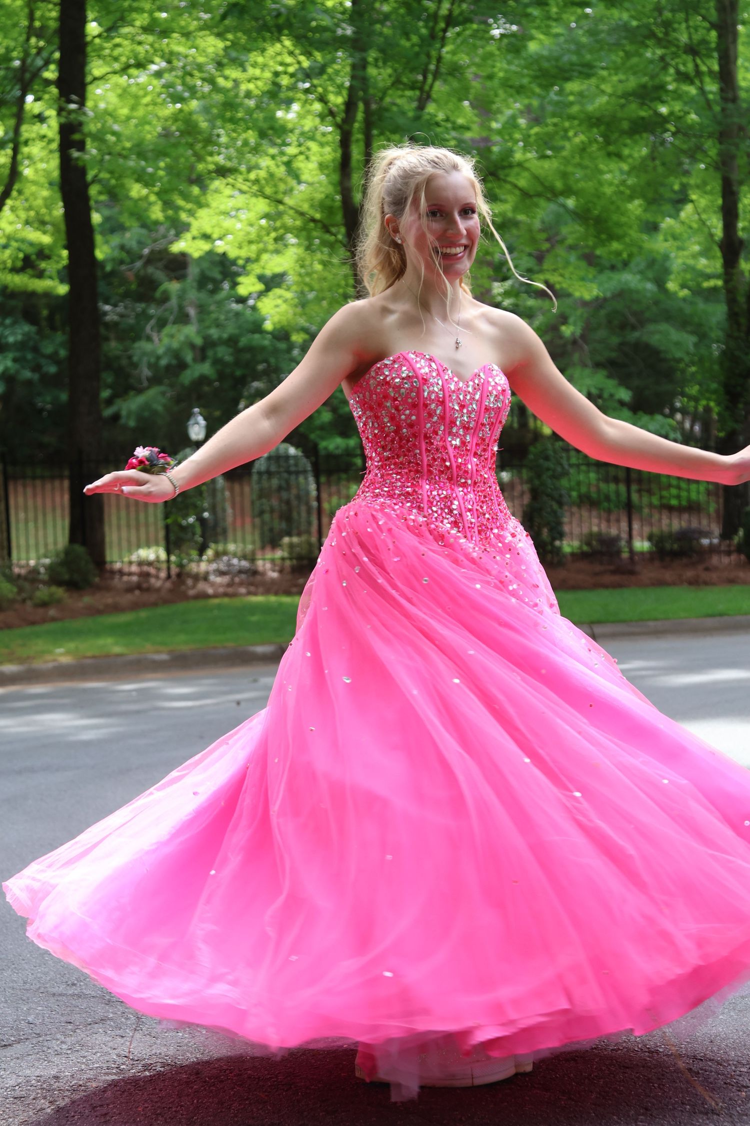 Teen twirls a flowing bright pink prom gown on a wooded driveway.