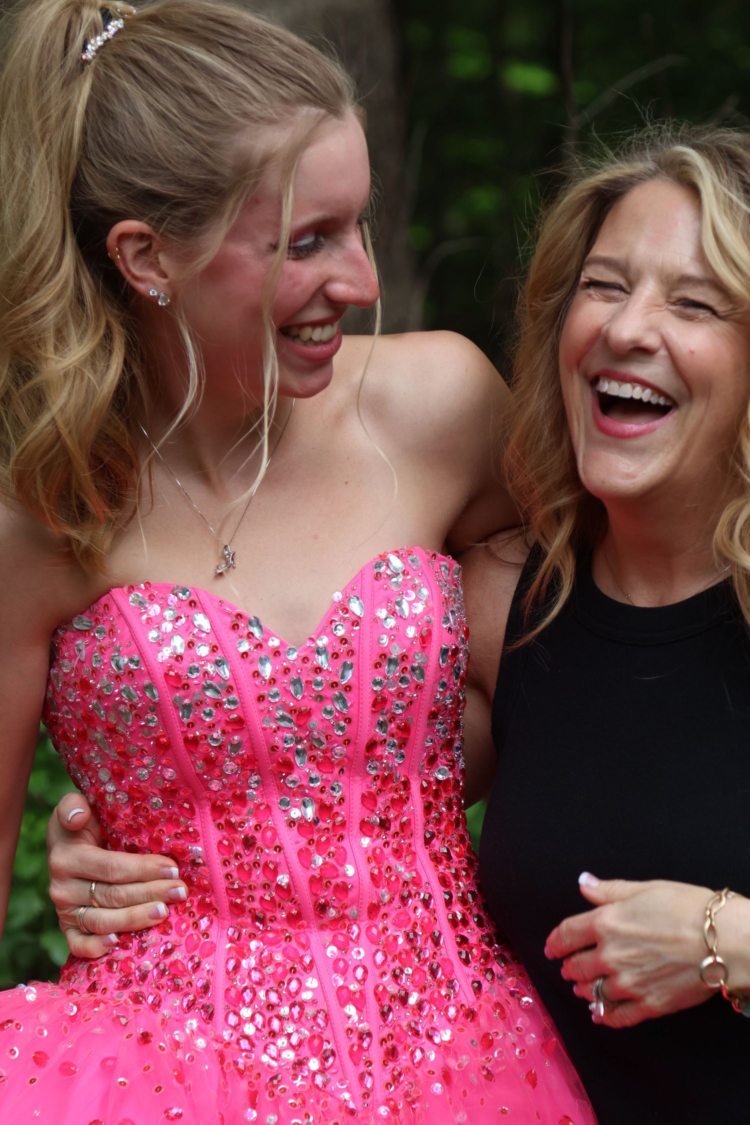 Teen in a bright pink prom gown laughs with mom dressed in black.