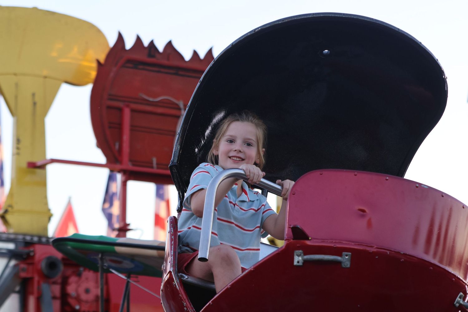 Young child smiles from a red carnival ride car.