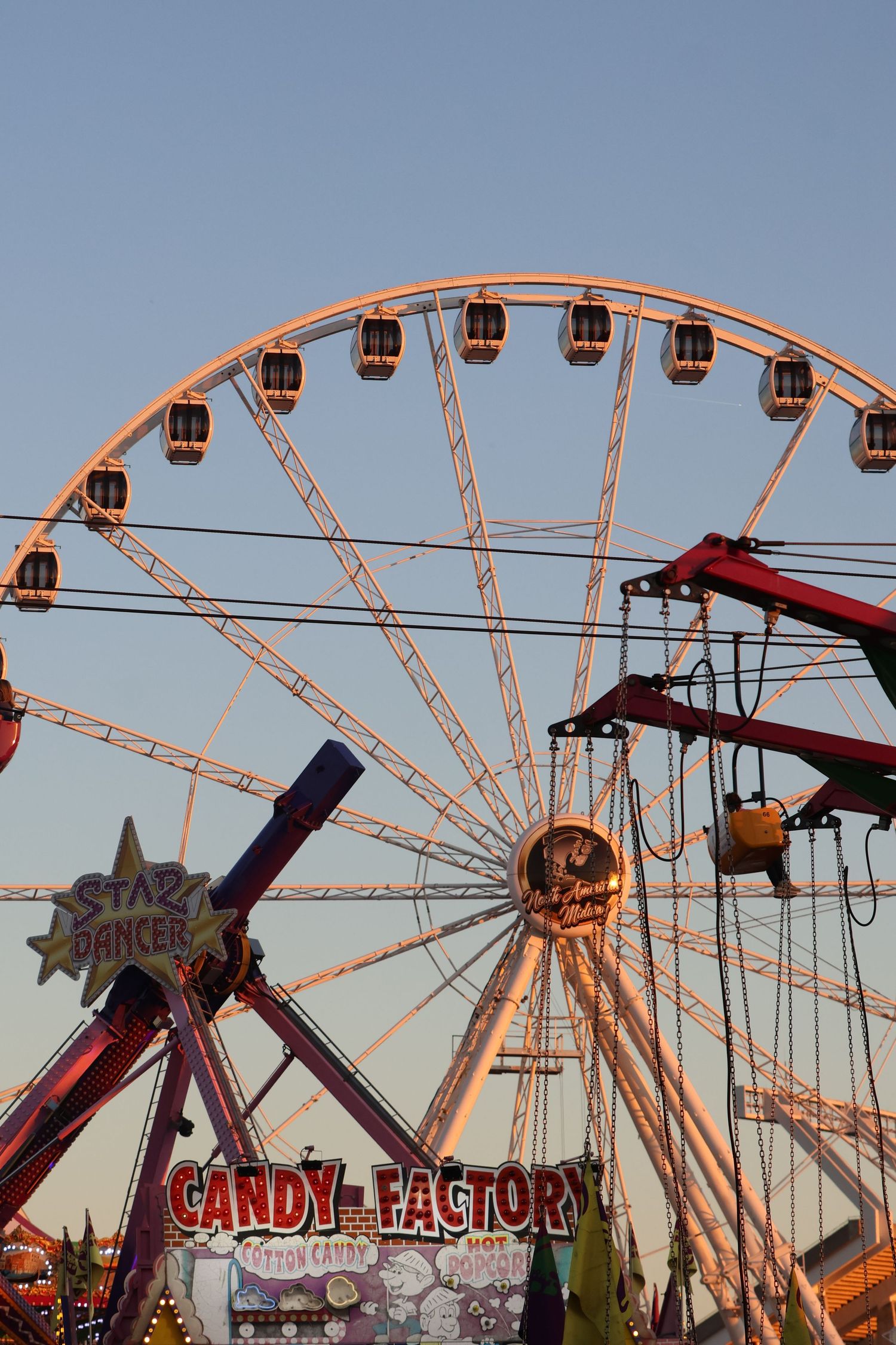 Ferris wheel and colorful carnival rides rise above a midway at dusk.