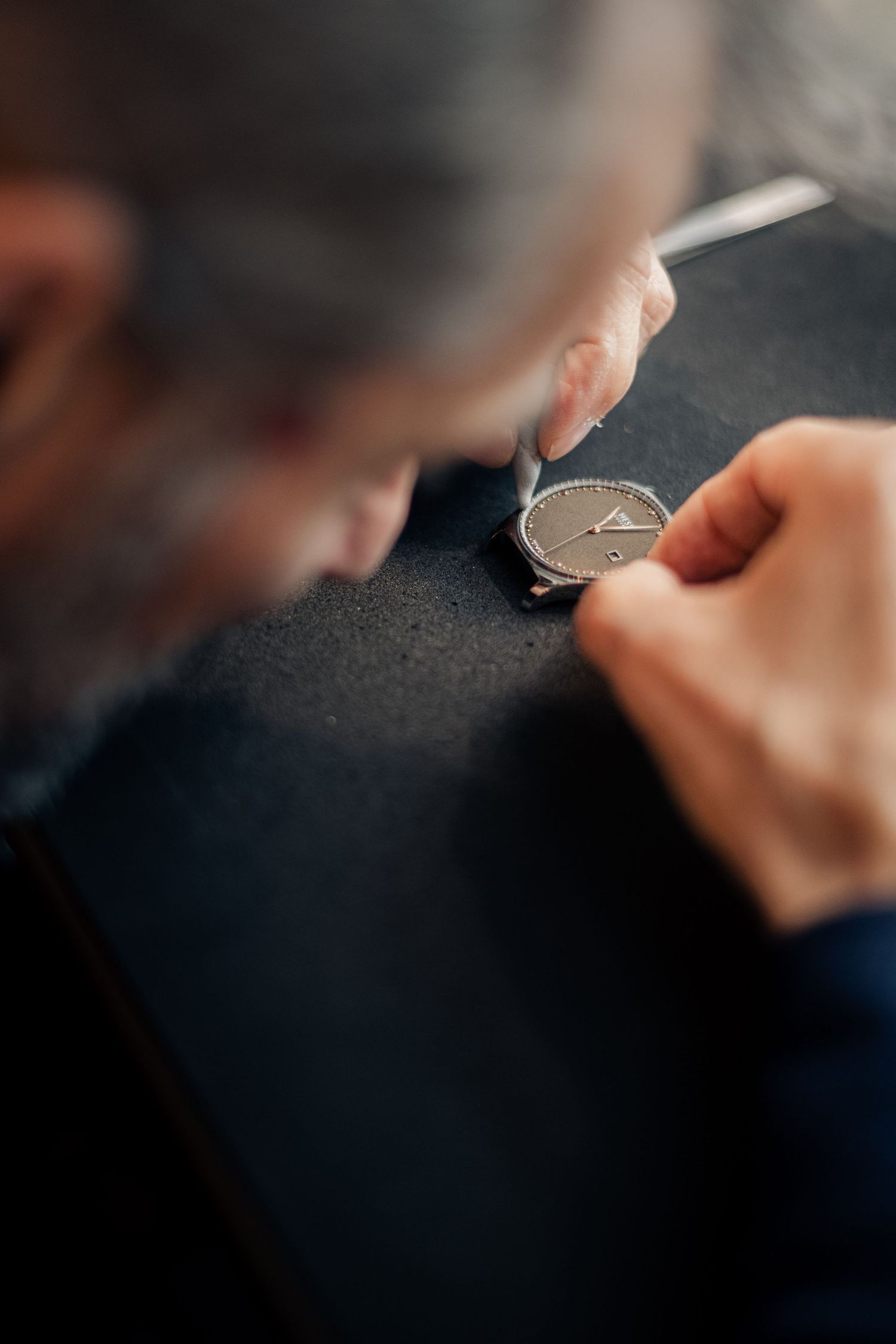 Detailed shot of hands working on watch mechanism repair against dark surface.