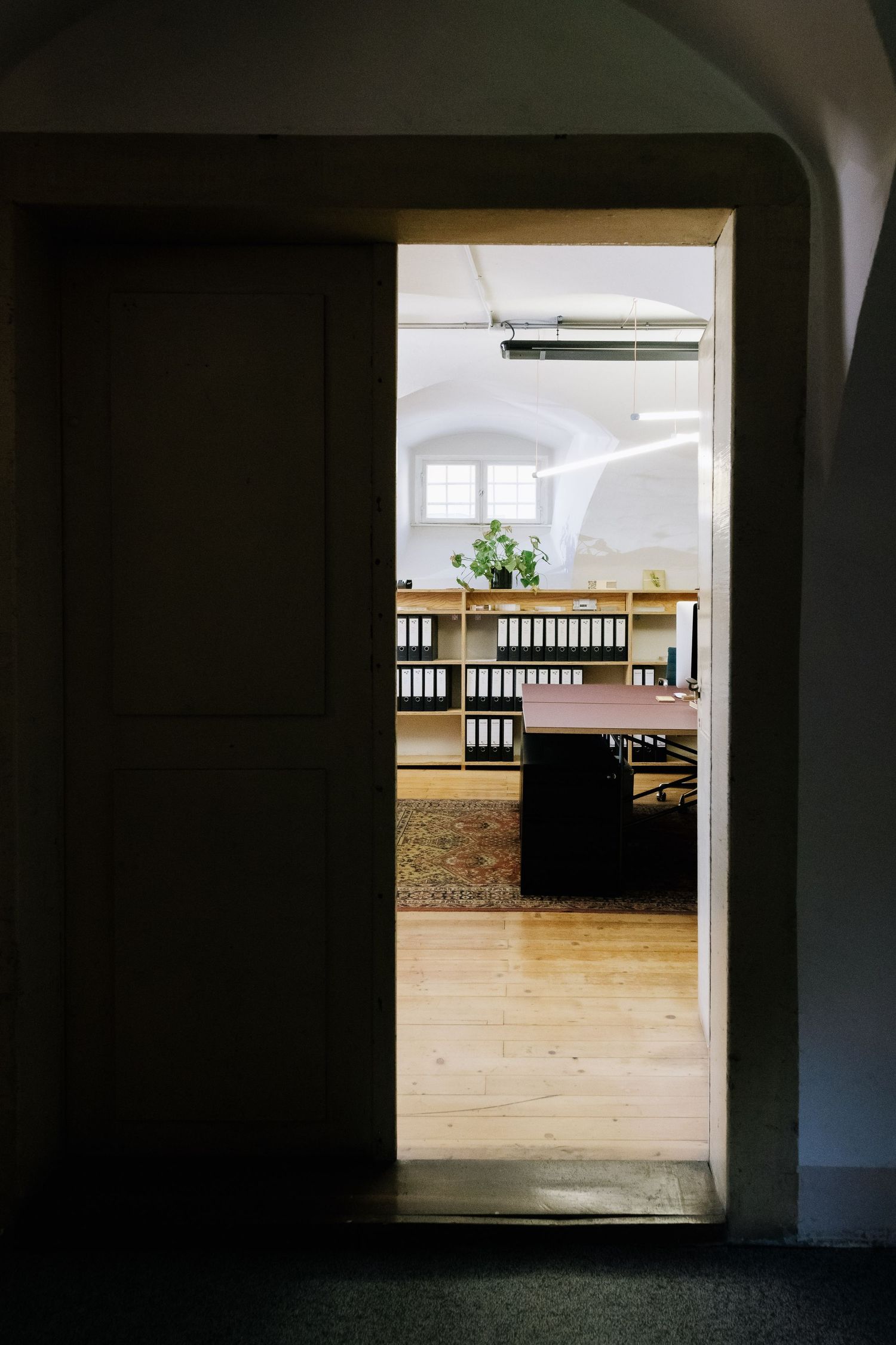 View through doorway into bright office space with wooden floors and file storage.