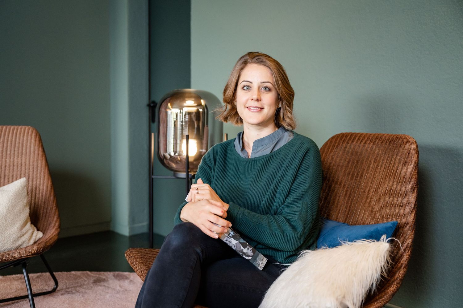 Casual office scene with person relaxing in brown armchair next to modern lamp fixture.