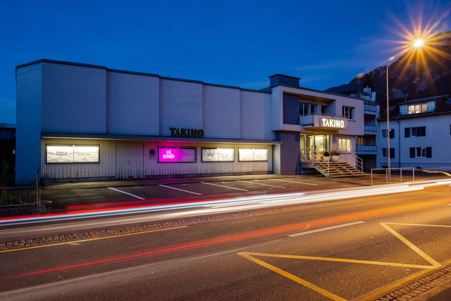 Modern building exterior at dusk with light trails from passing cars on street.