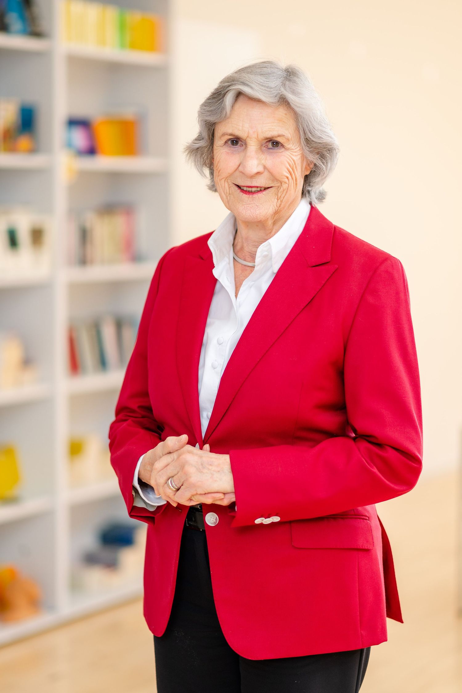 Professional wearing bright red blazer standing in front of organized bookshelf.