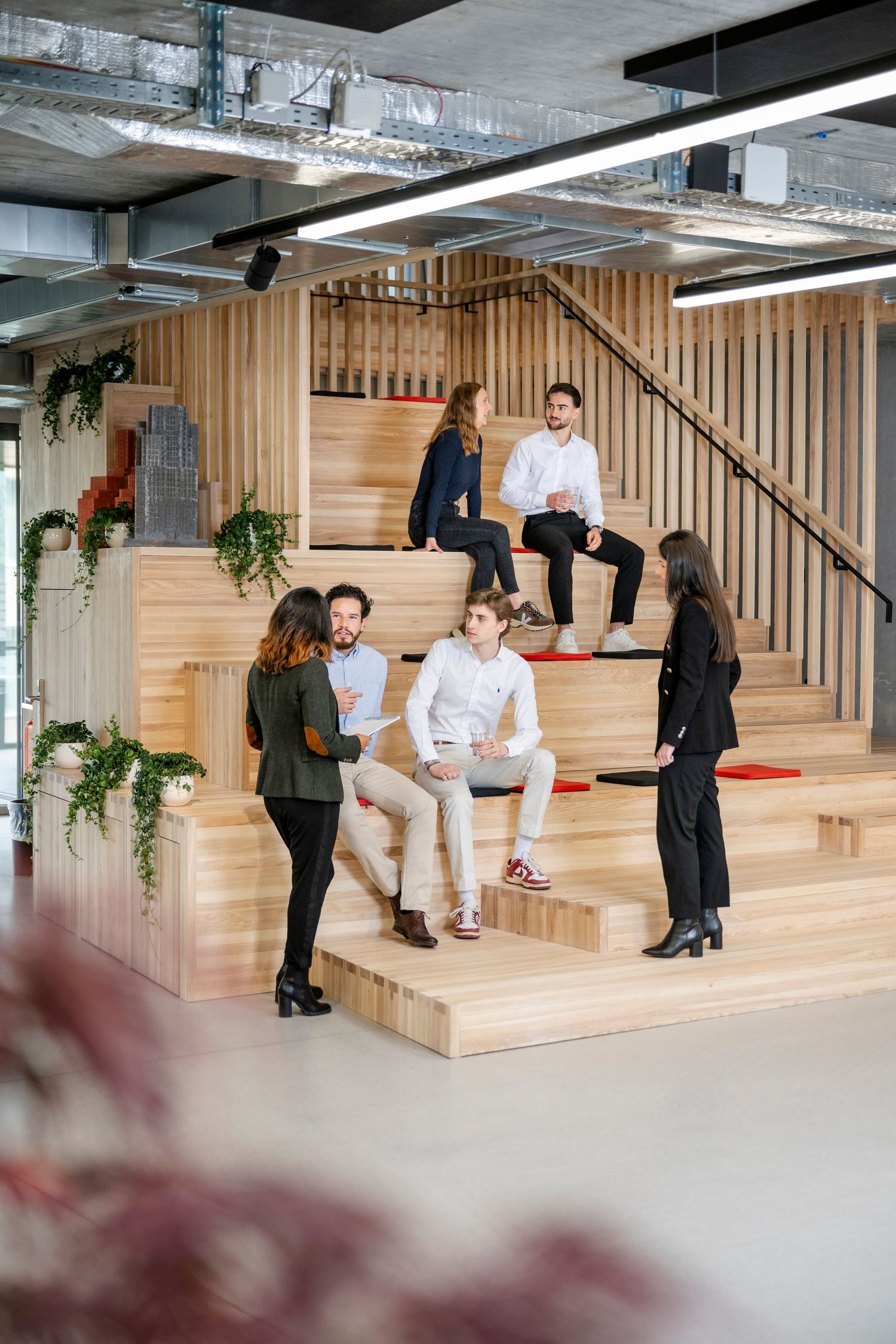 Modern office with wooden stadium seating steps where colleagues gather for informal meeting.
