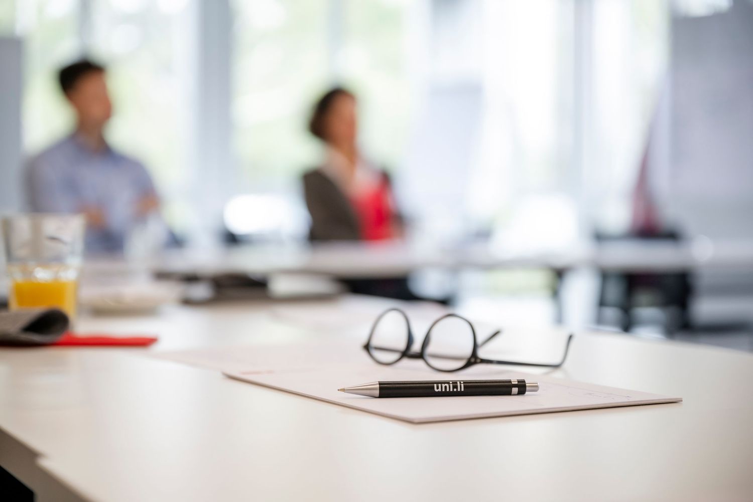 Blurred office meeting room with eyeglasses and pen on conference table.
