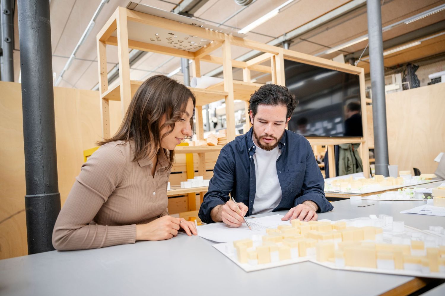 Colleagues collaborate on architectural plans at workspace desk.