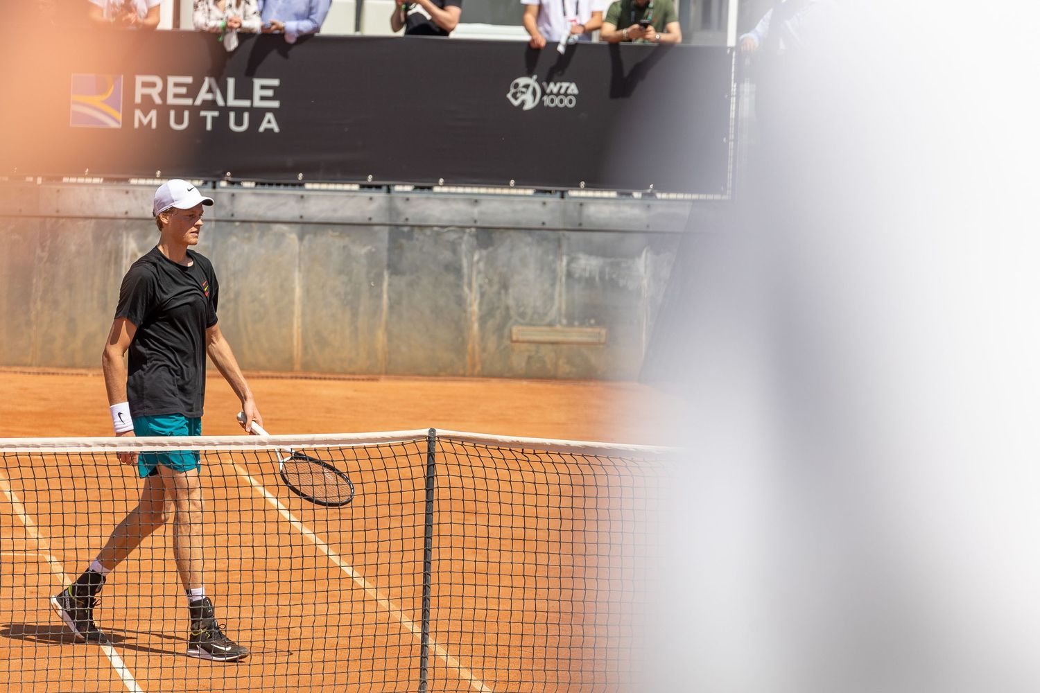 Tennis player walking past clay court net during match at outdoor tournament.