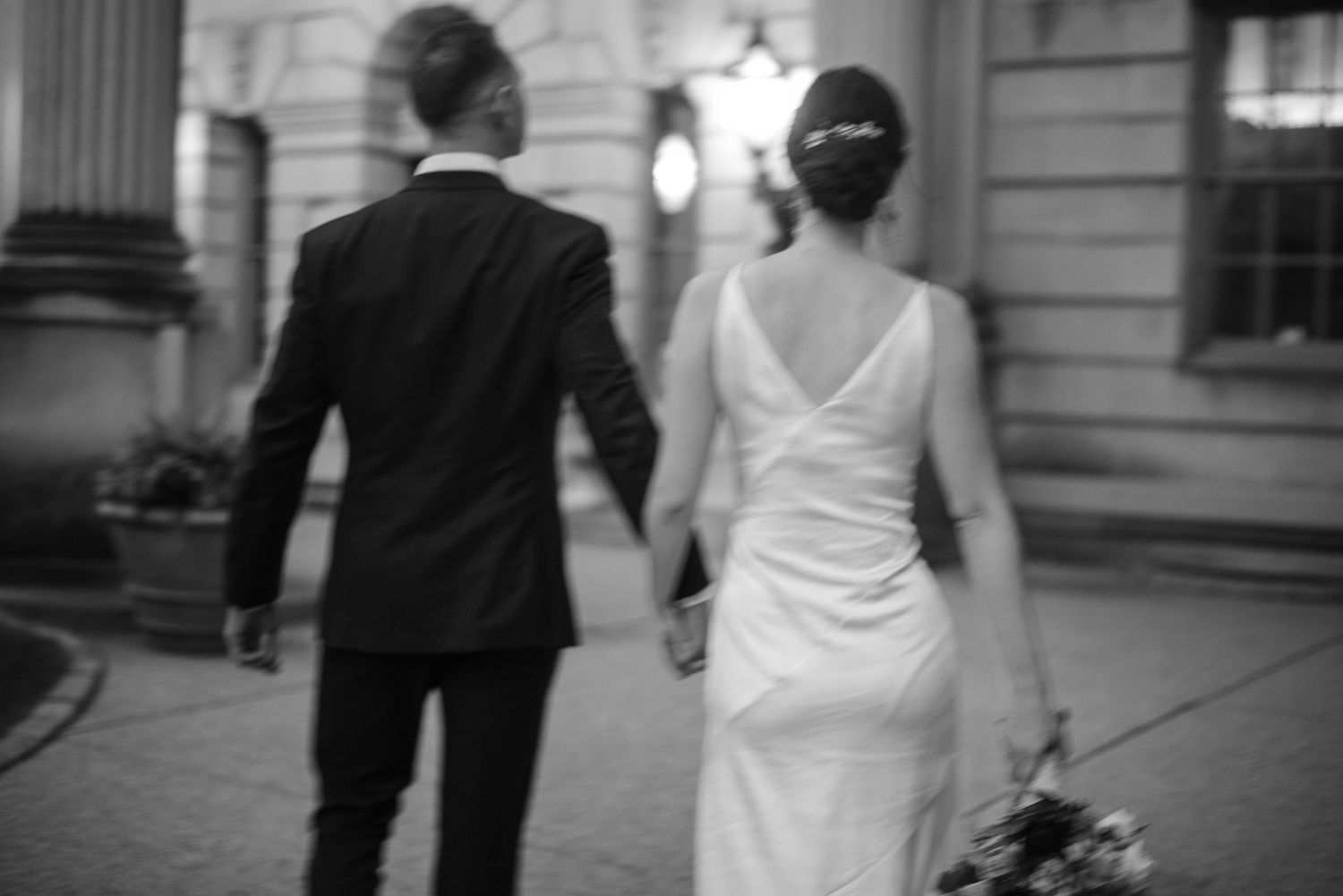 Blurred black and white photo of couple walking hand in hand along city street.