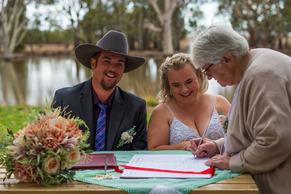 Wedding ceremony participants signing official documents at outdoor lakeside venue.