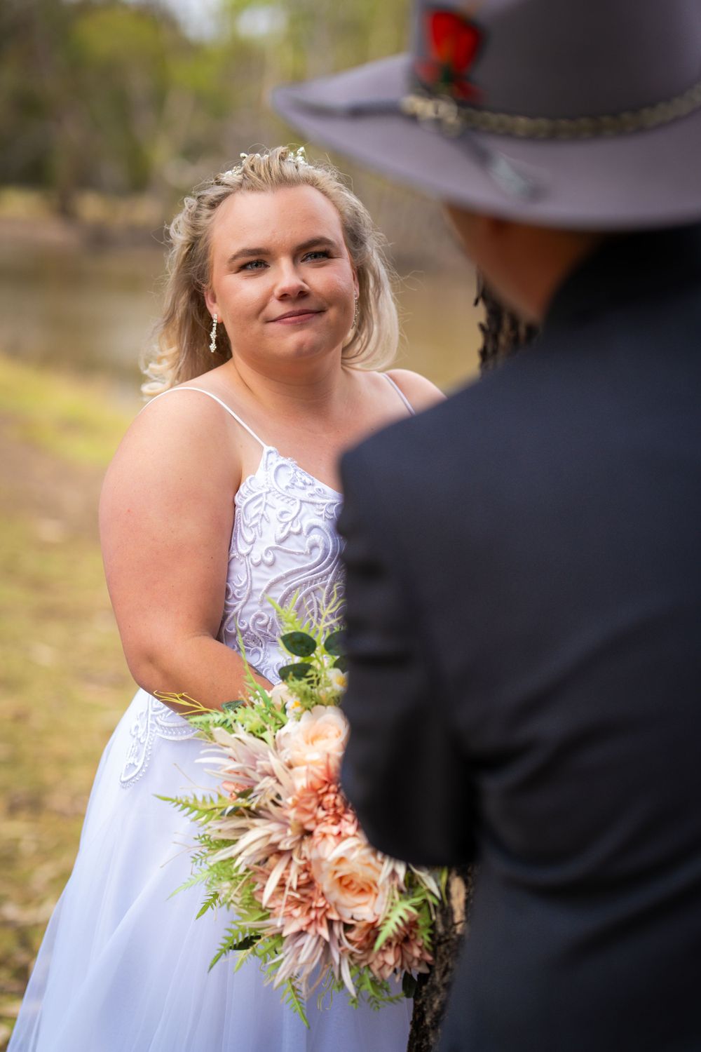 Bride holding peach bouquet during outdoor wedding ceremony.