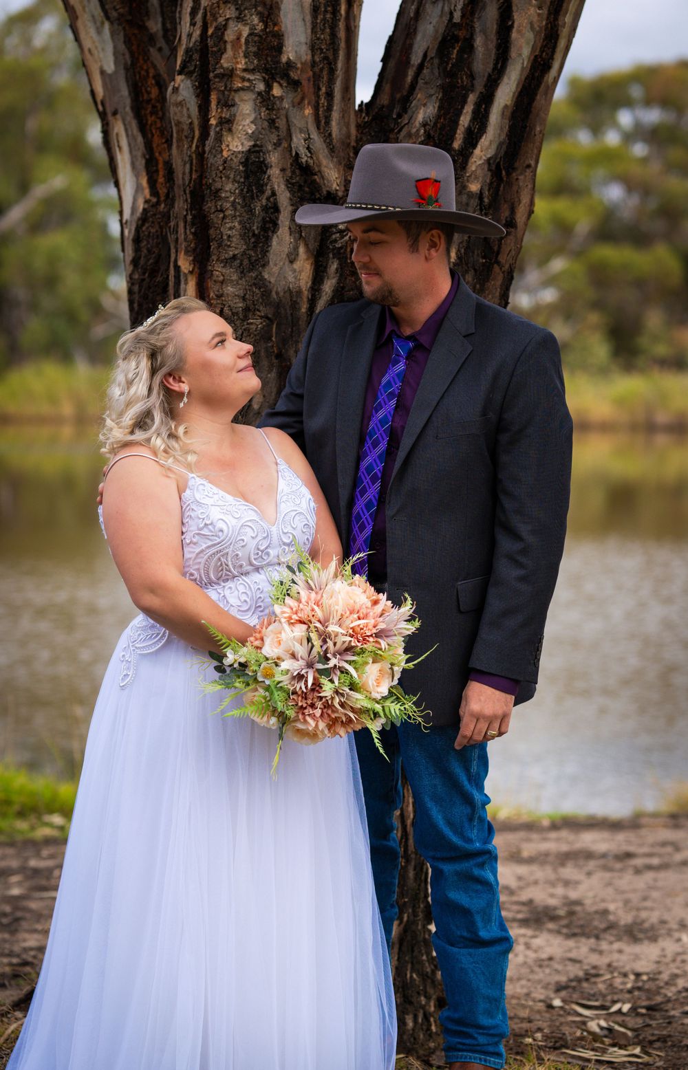 Romantic moment between newlyweds by lake with eucalyptus trees in background.