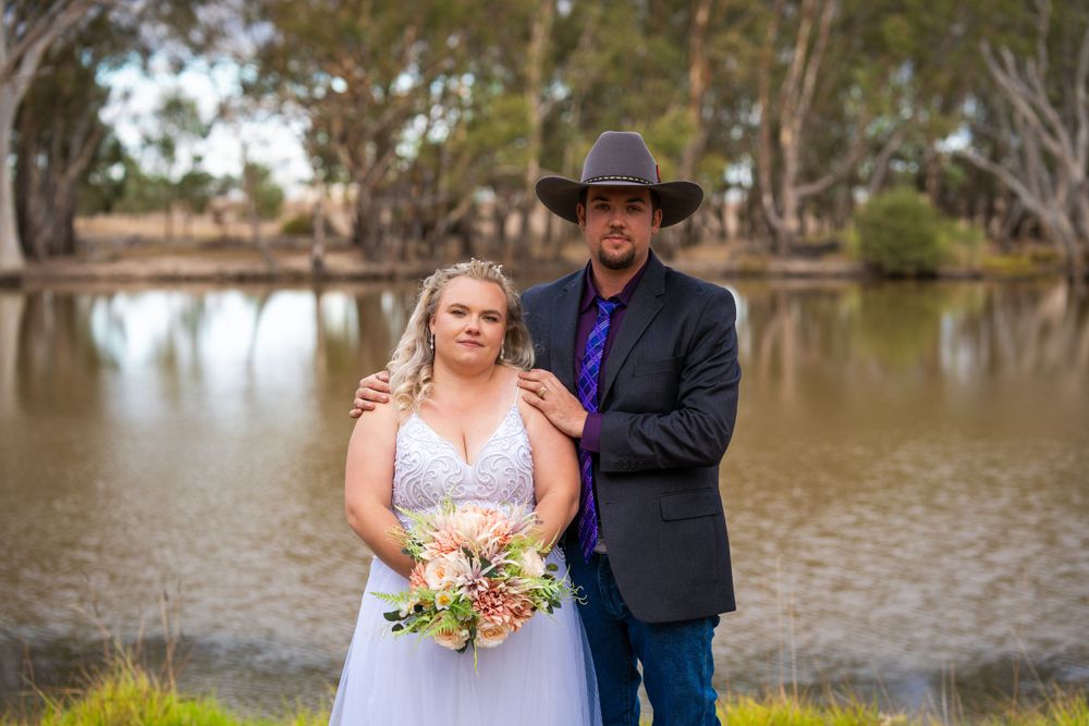 A romantic wedding photo of a couple posing by a tranquil pond with gum trees in the background.