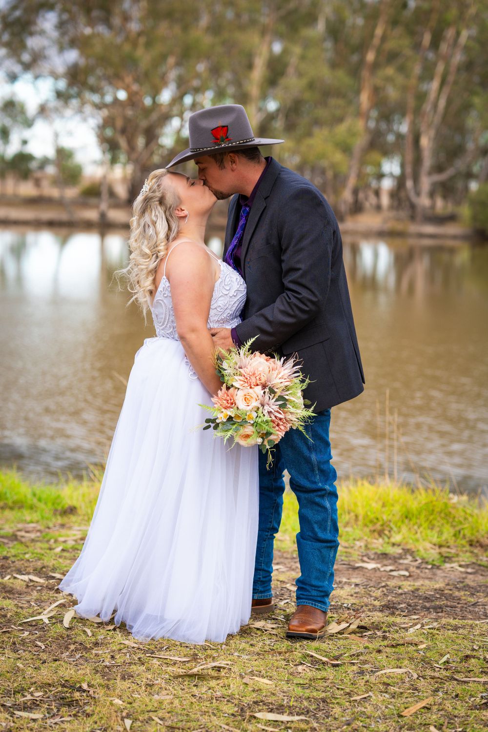 A tender wedding moment captured by a lake with eucalyptus trees framing the scene.