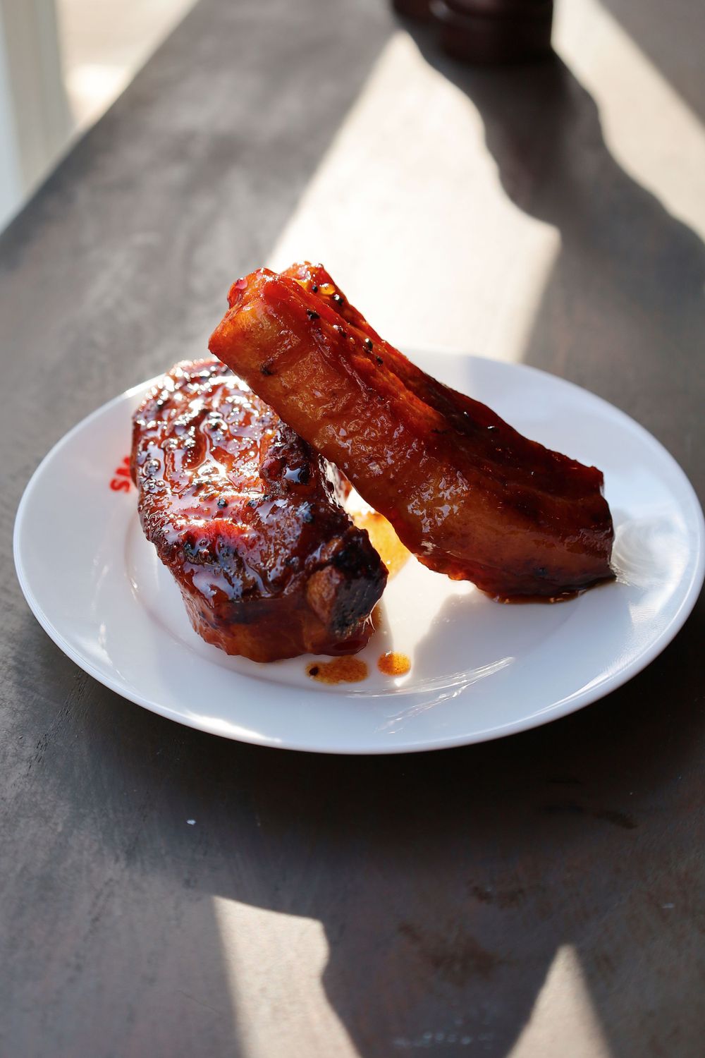 Grilled barbecue ribs with sauce on white plates photographed in dramatic lighting.