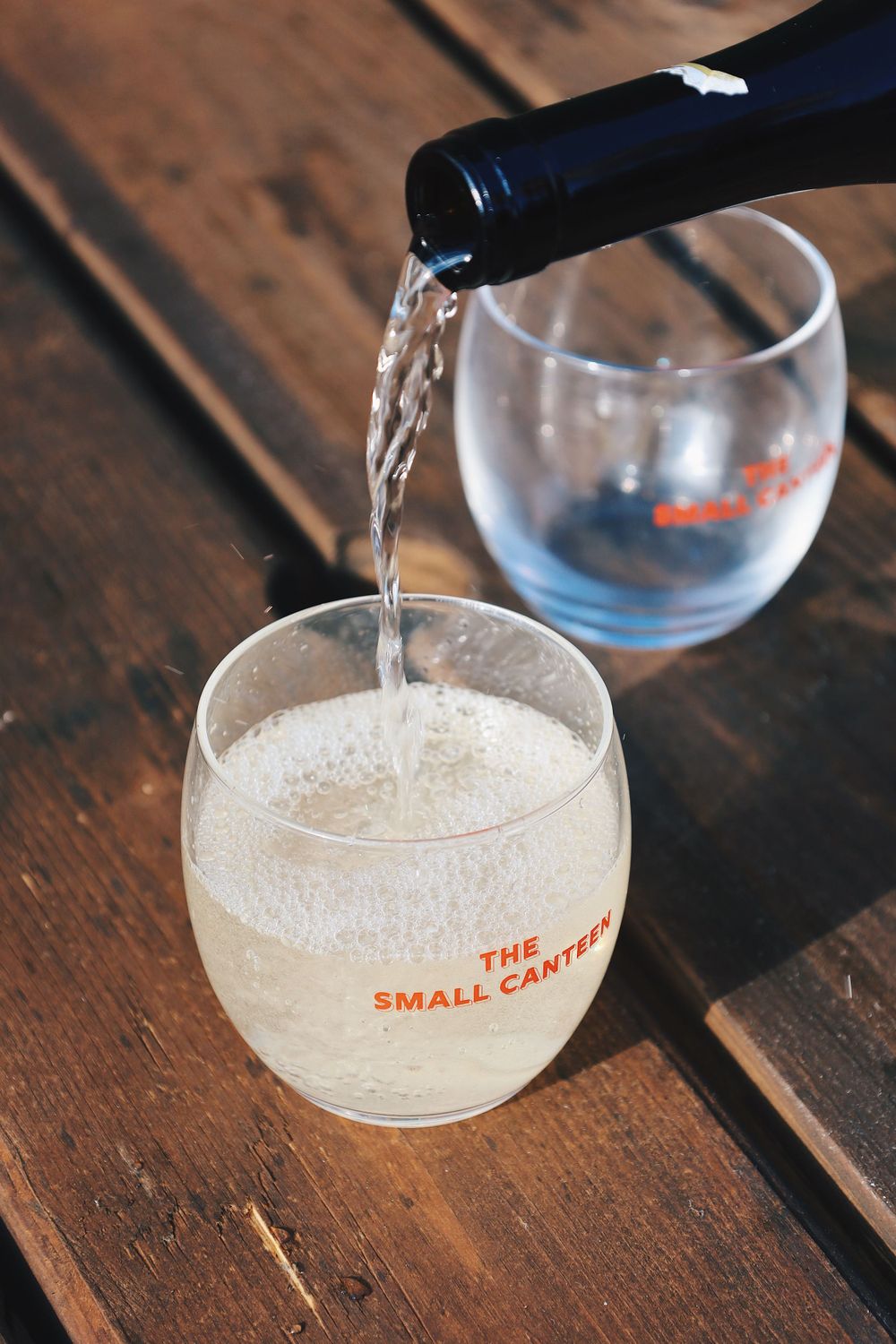 Sparkling wine being poured into branded glassware on a wooden table.