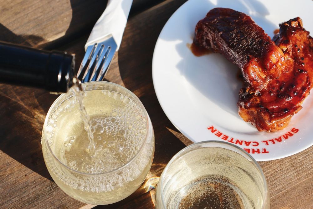 Sparkling drinks and grilled meats arranged on a dark wooden table surface.
