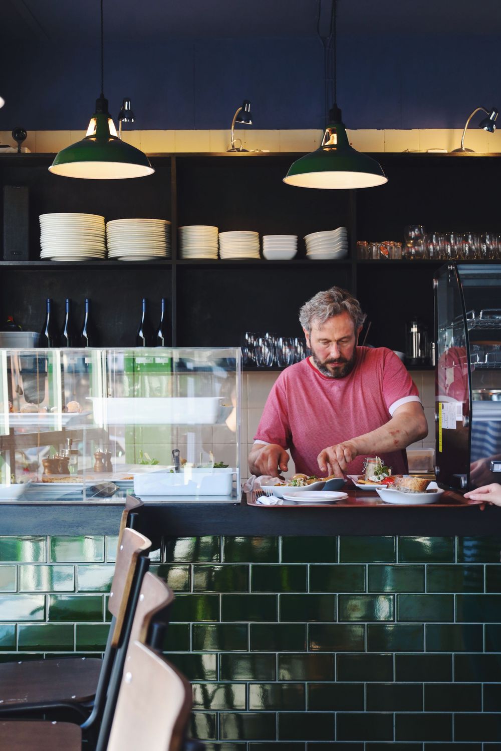 Modern restaurant interior with green tiled walls and pendant lighting over the bar area.