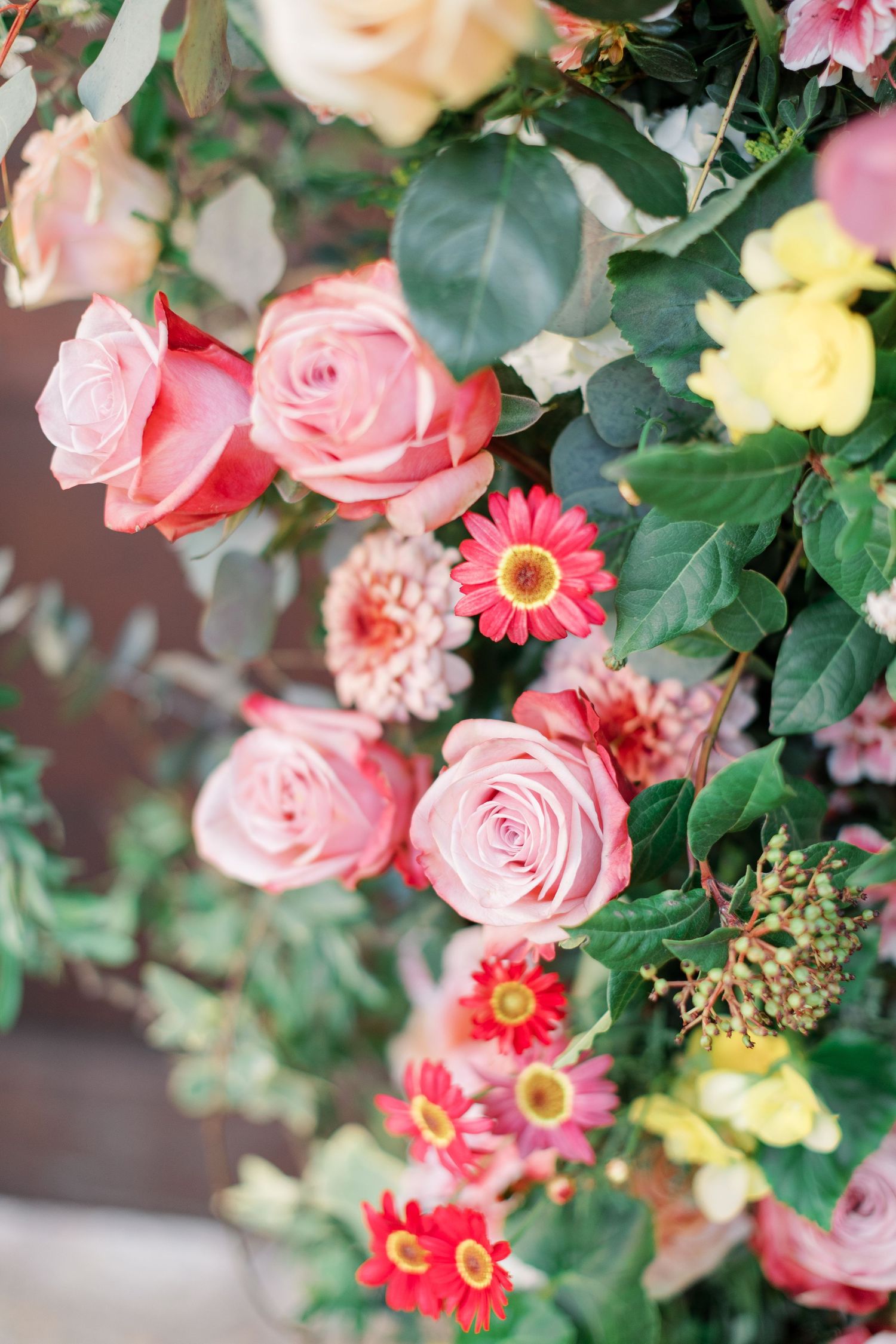 Pink roses and red gerbera daisies create a vibrant floral arrangement with lush green foliage.