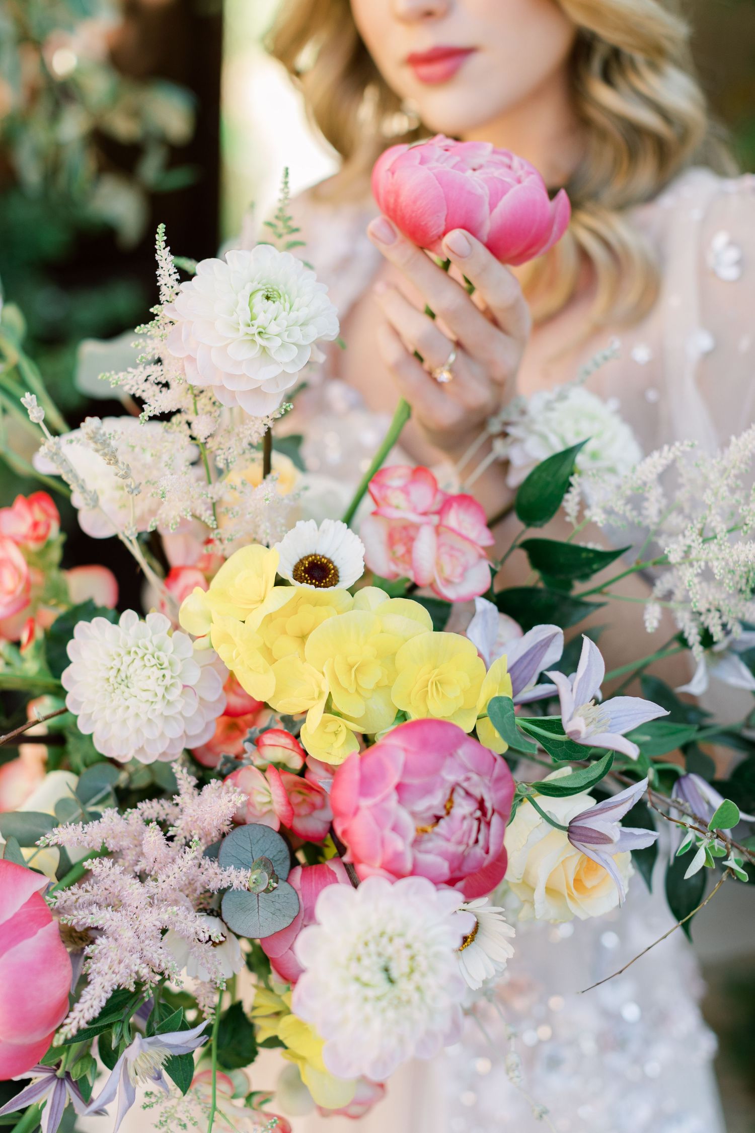 Romantic floral arrangement with yellow roses, pink peonies and white blooms held against a lace dress.