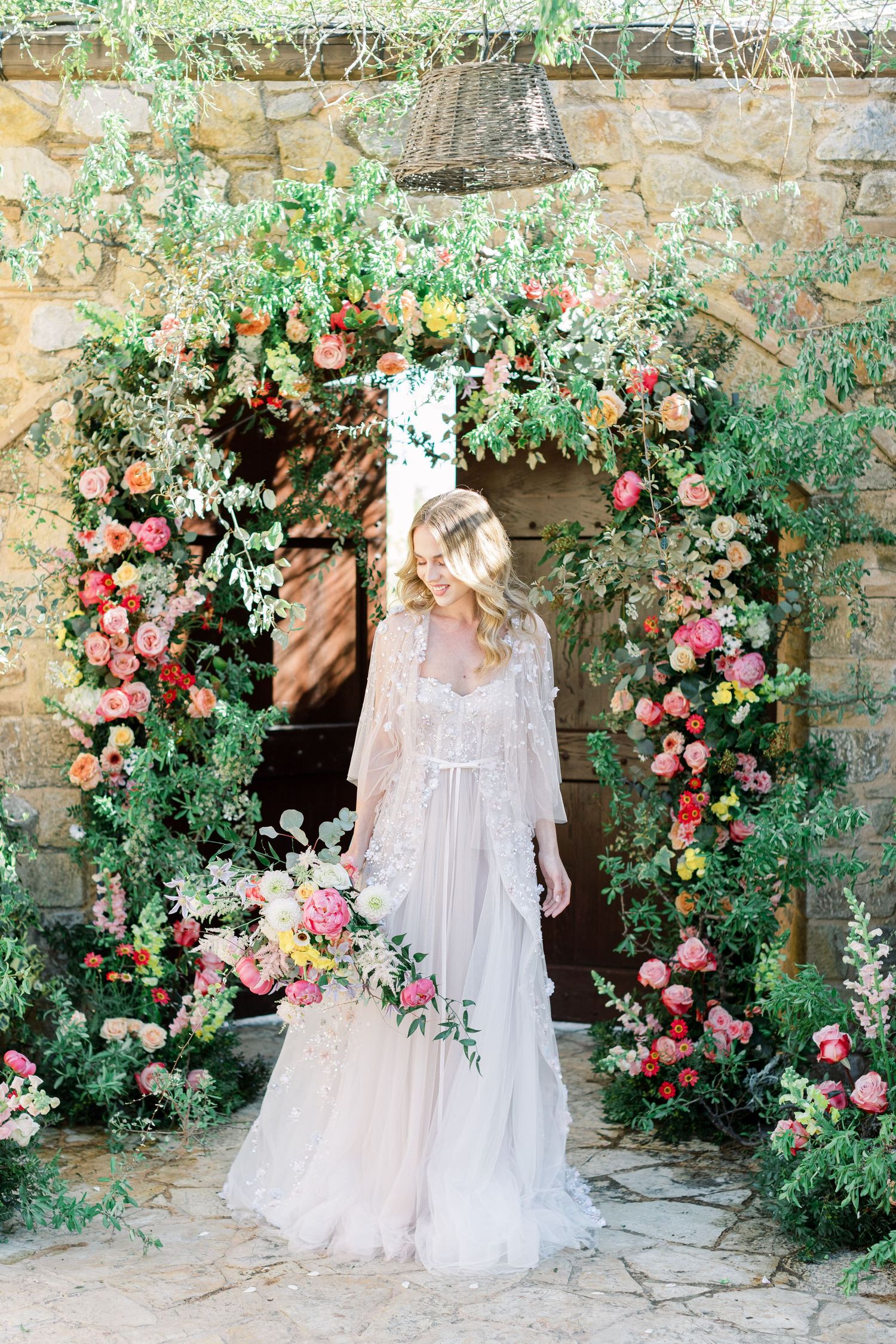 Romantic floral archway covered in pink roses and greenery frames an ethereal white lace wedding gown.